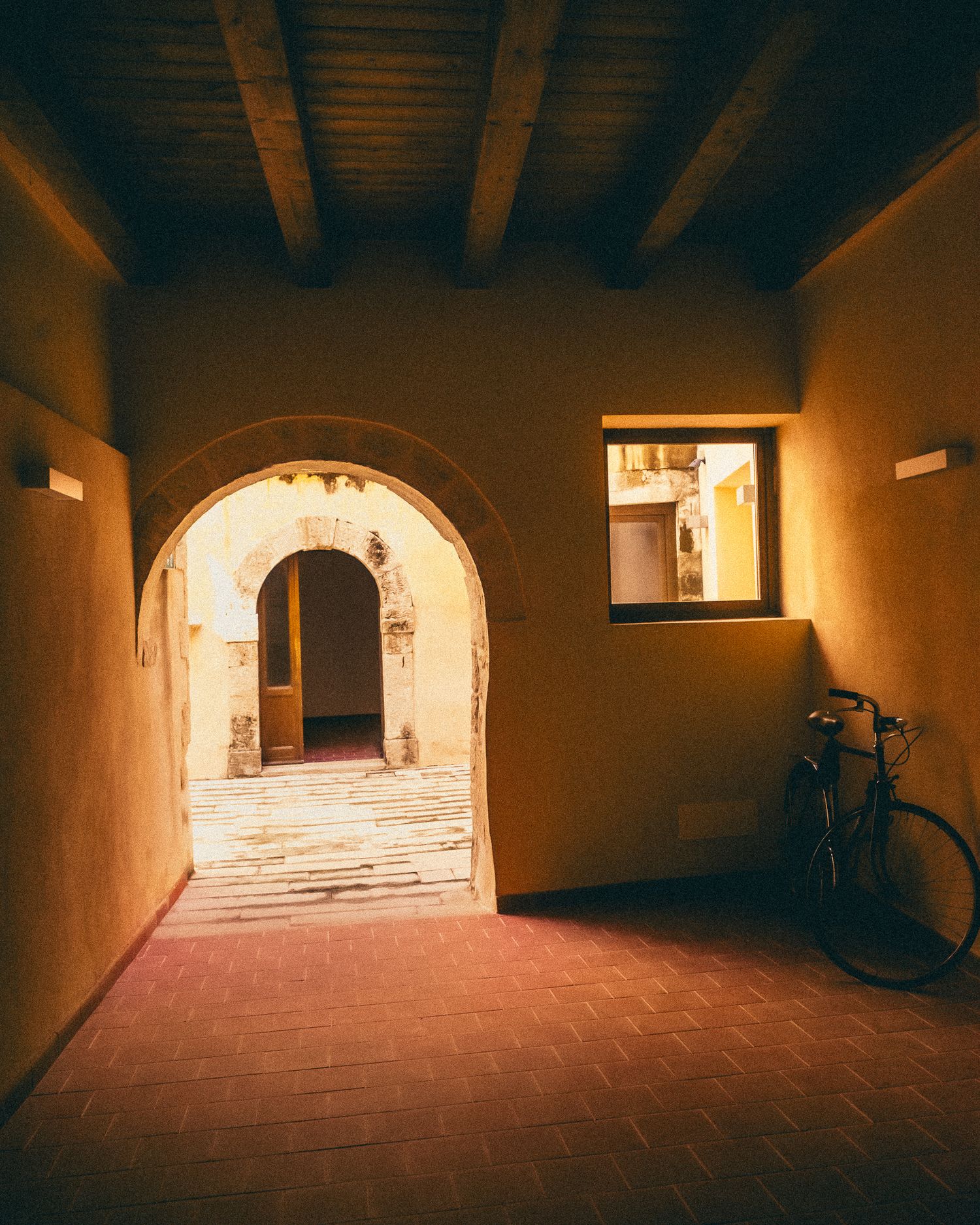 A panoramic view of a dimly lit stone corridor with arched doorways and wooden beams on the ceiling.