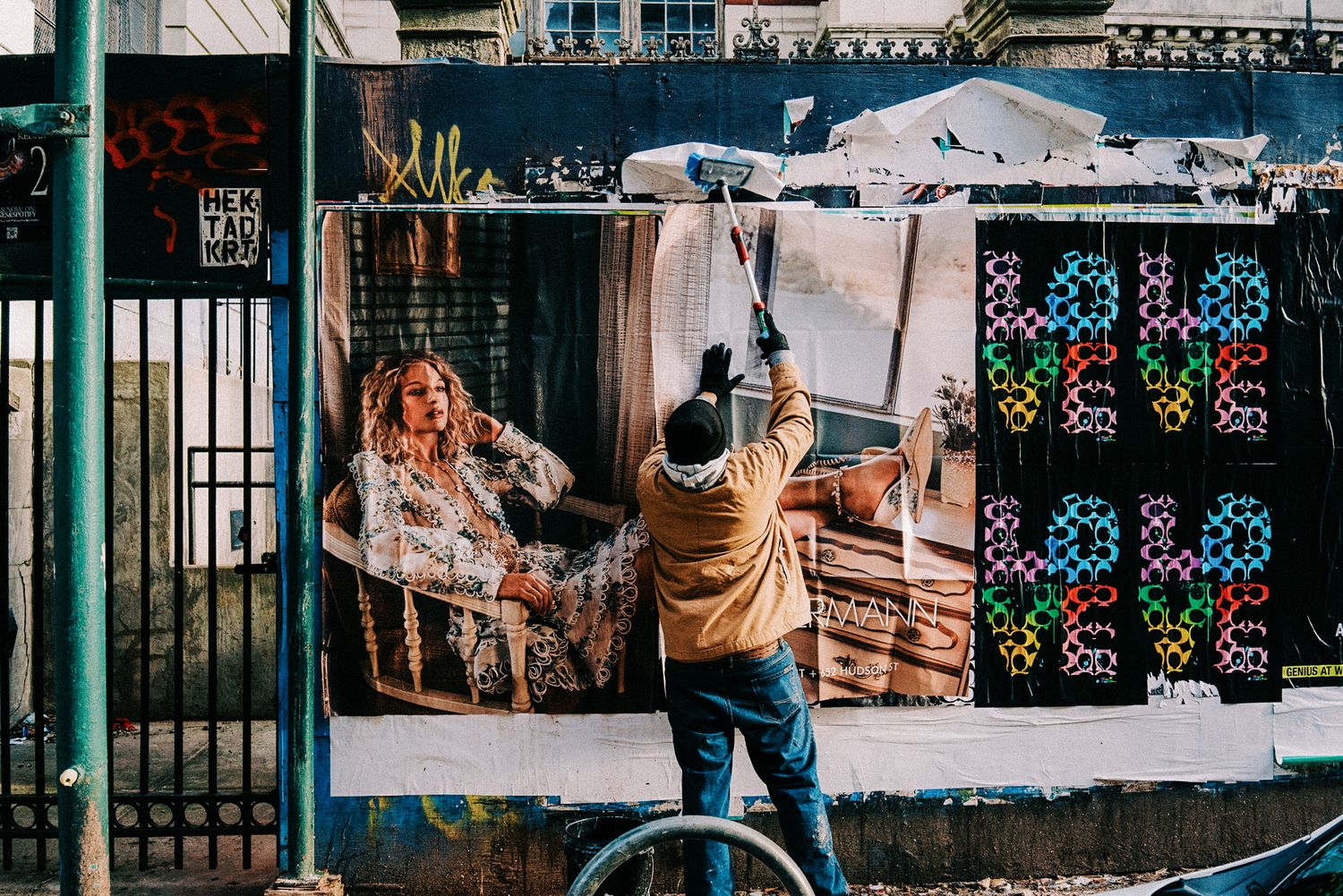 Man posting a large advertisement on an outdoor wall covered in graffiti and street art in an urban setting.
