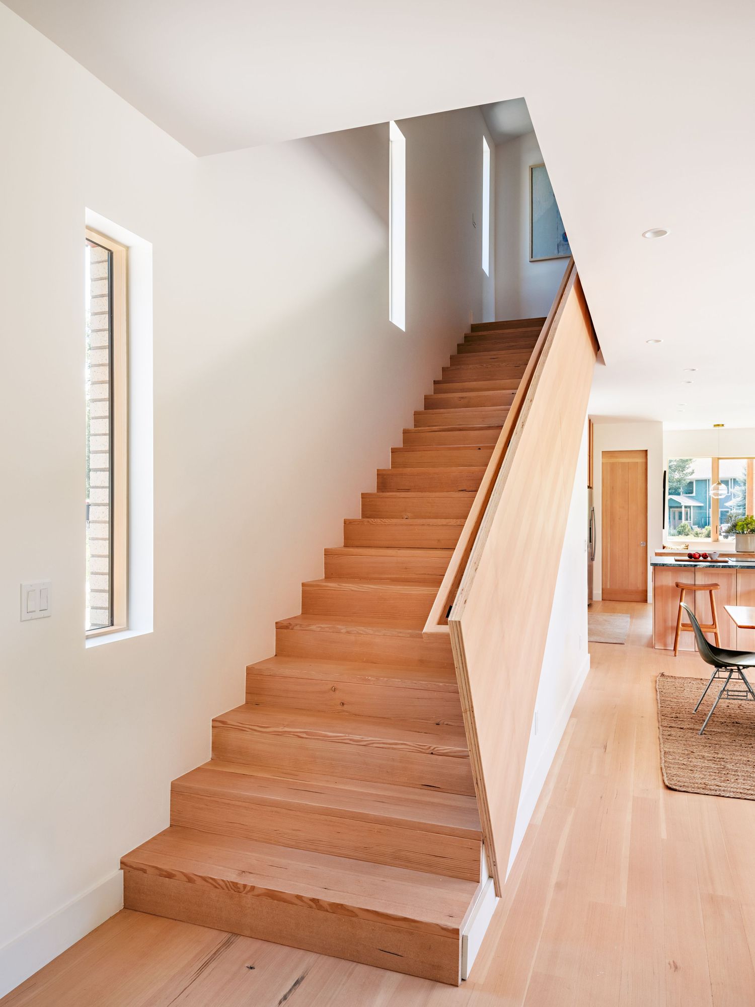 Minimalist wooden staircase with white walls and natural light flowing through windows creates an airy atmosphere.