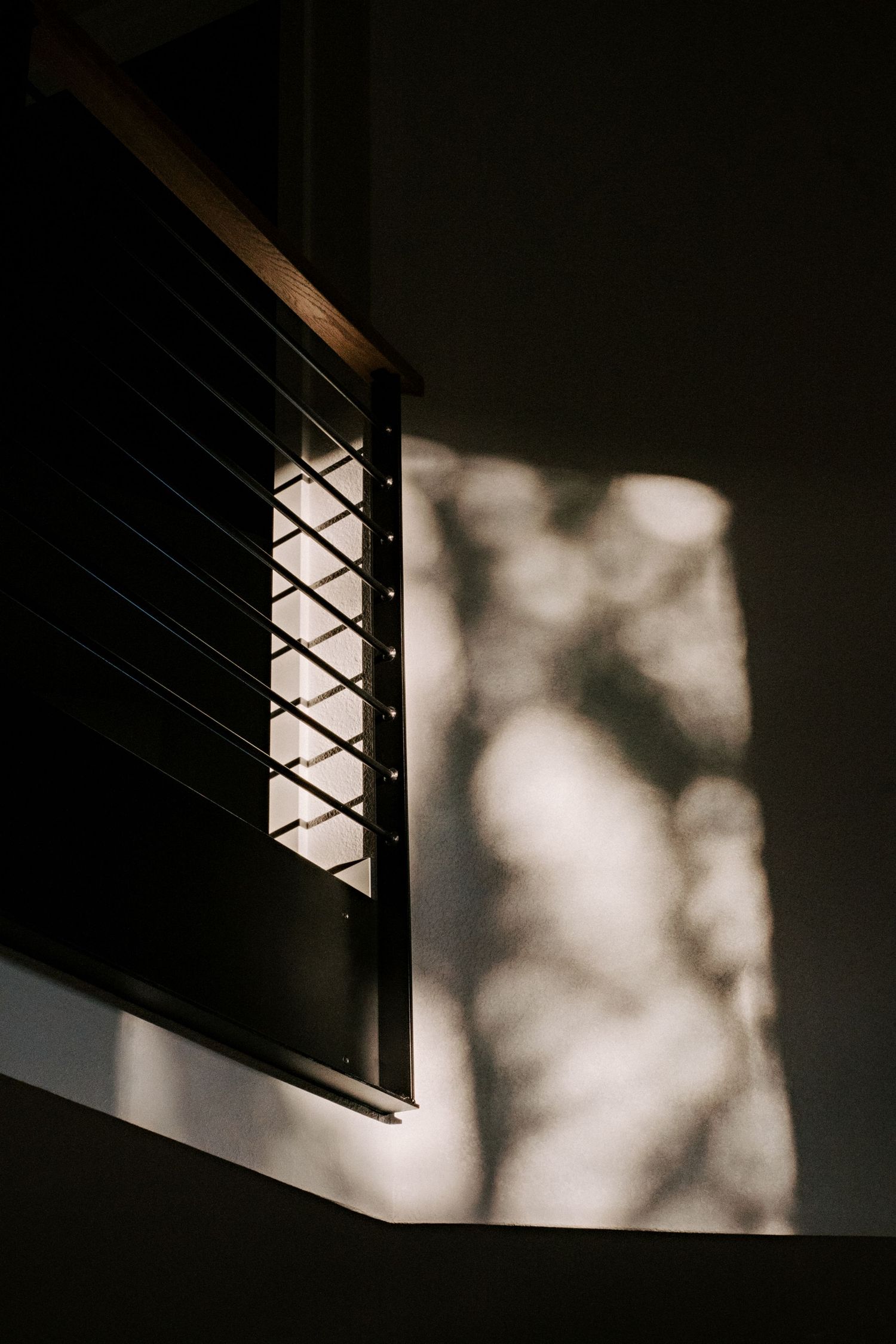 Artistic shadow patterns cast through window grating onto a white interior wall.