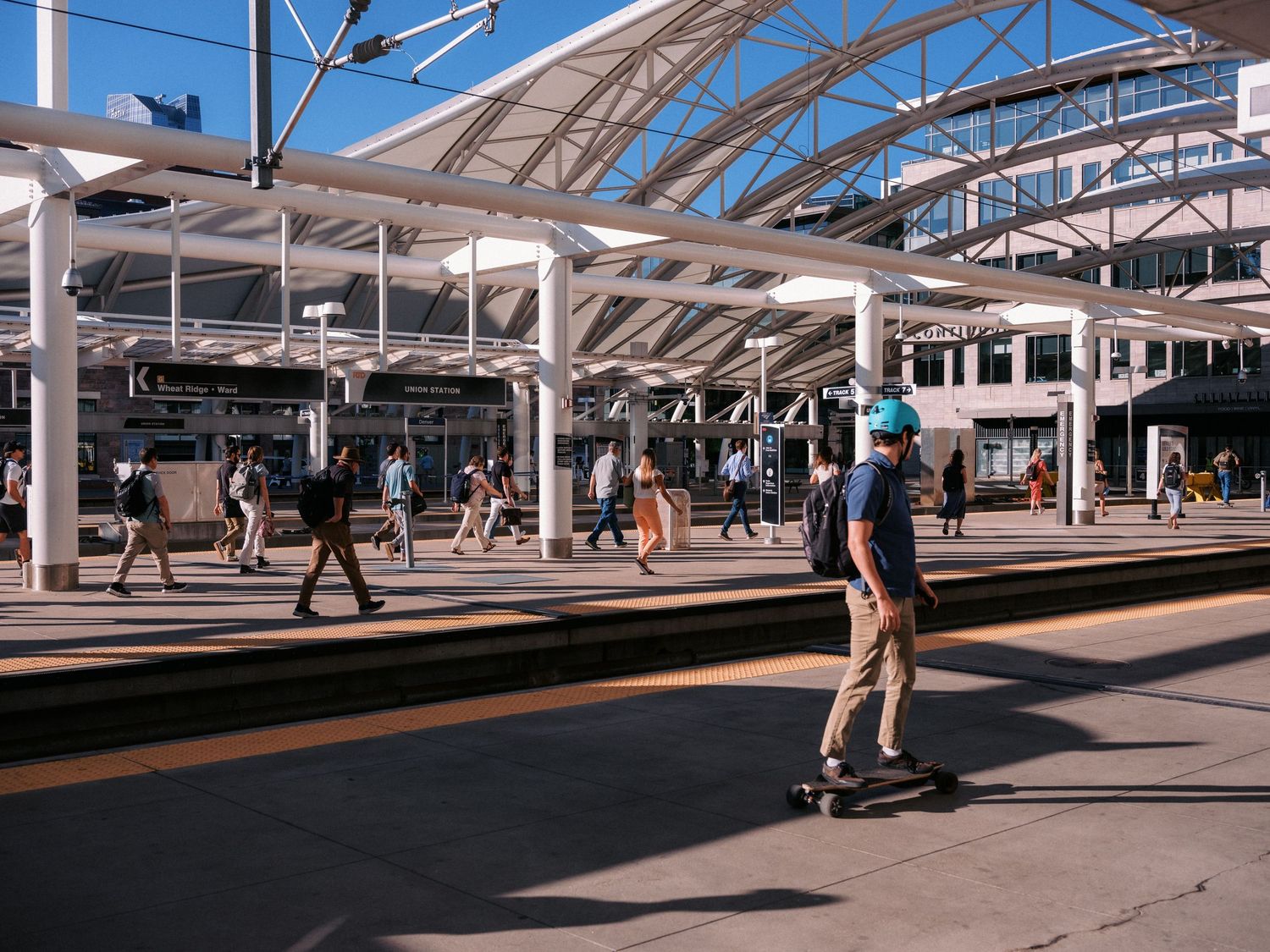 Train station platform with covered walkway and passengers waiting during daytime.