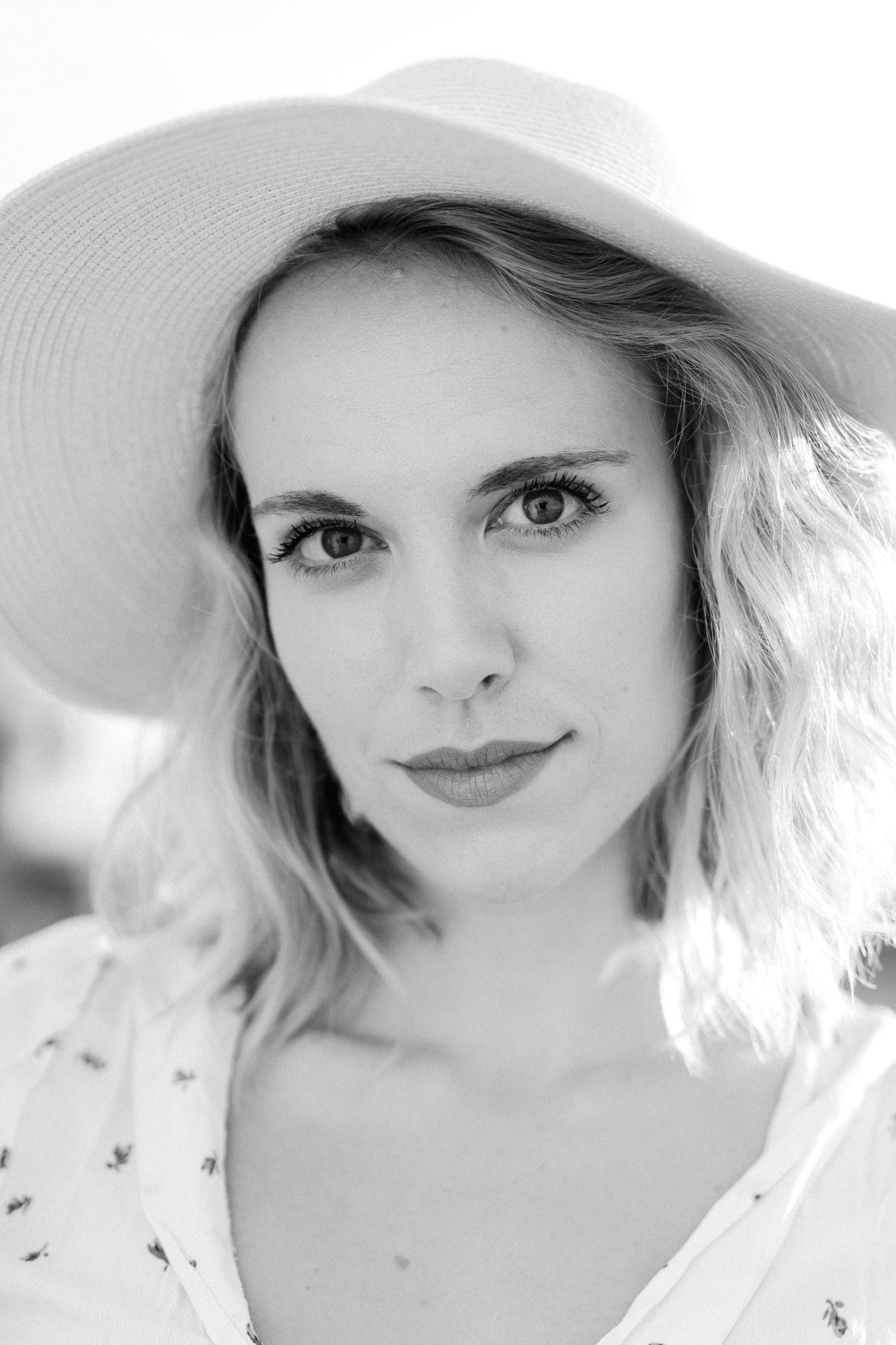Elegant portrait of someone in a wide-brimmed white sun hat with soft lighting.