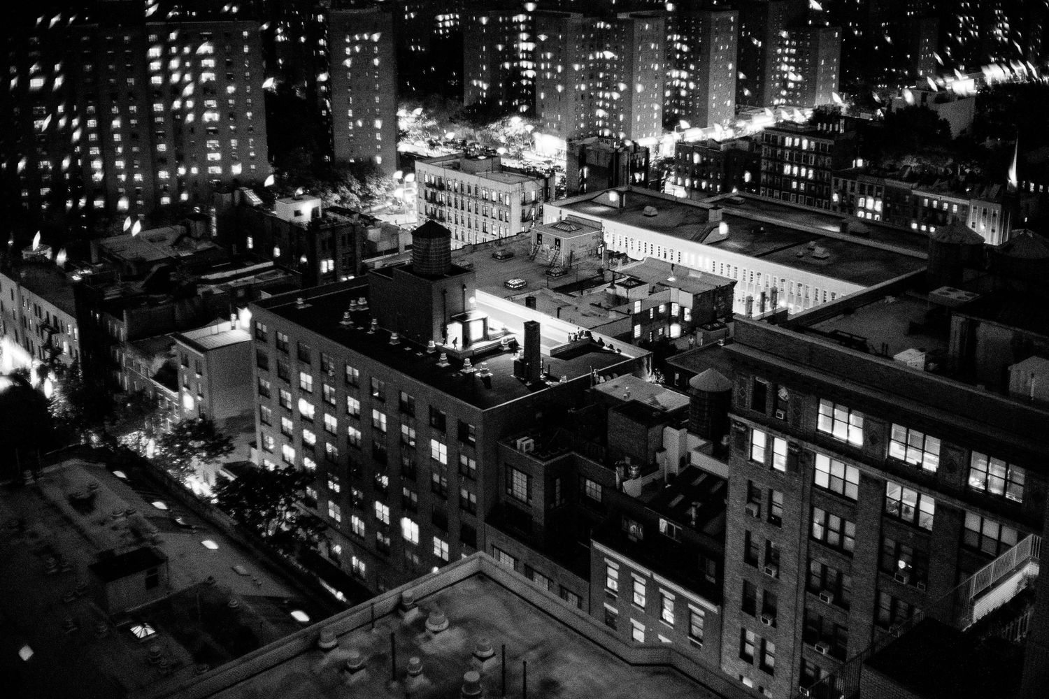 Aerial black and white cityscape view of New York City buildings and streets at night with illuminated windows.