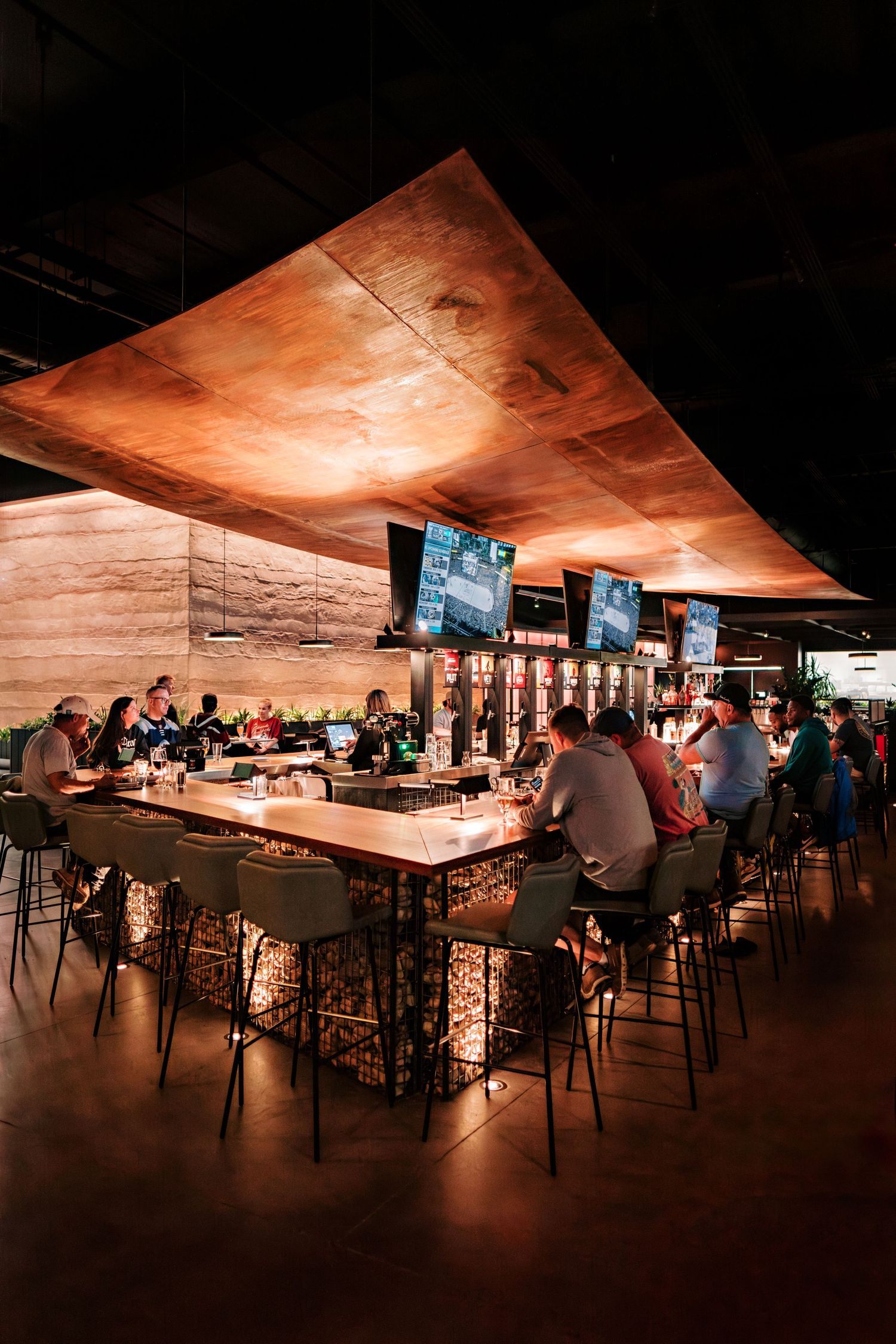 Warm-lit bar area with copper-toned ceiling and multiple screens displaying sports content.