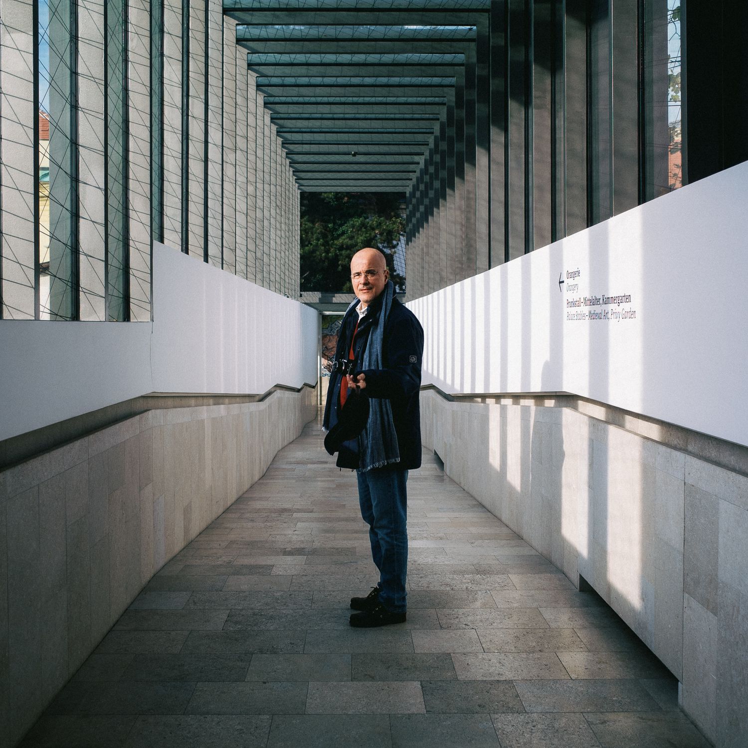 Figure standing in modern architectural corridor with repeating columns and dramatic lighting.