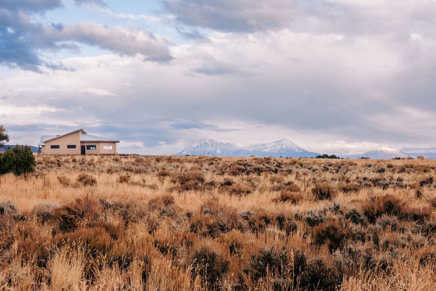 Wide desert landscape view with sagebrush and distant mountains under cloudy skies.