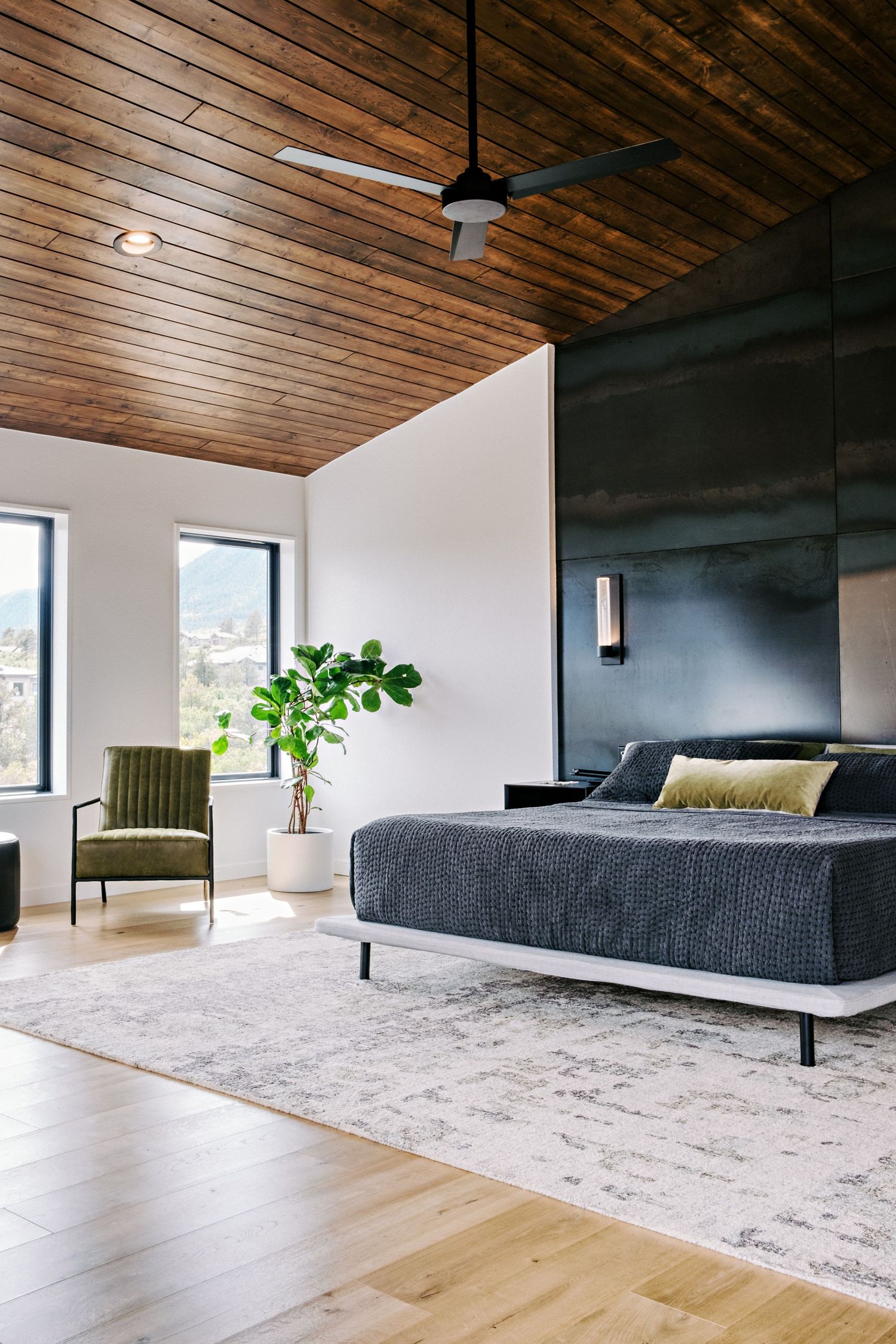 Contemporary bedroom with wooden ceiling, gray bedding, and large windows offering natural light.