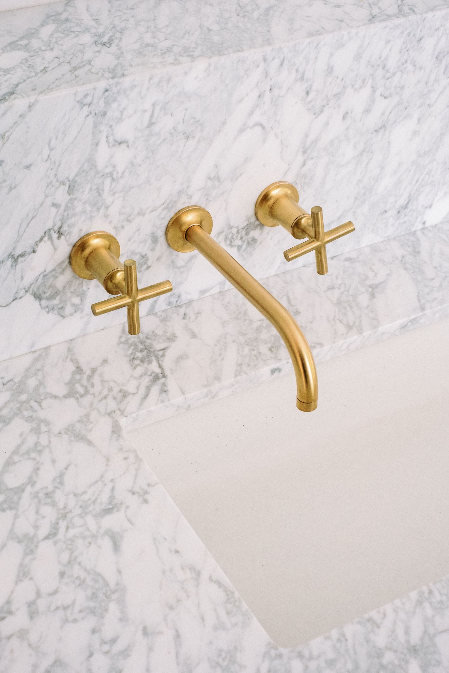 Elegant bathroom fixtures featuring brushed gold wall-mounted faucets against marble backsplash.