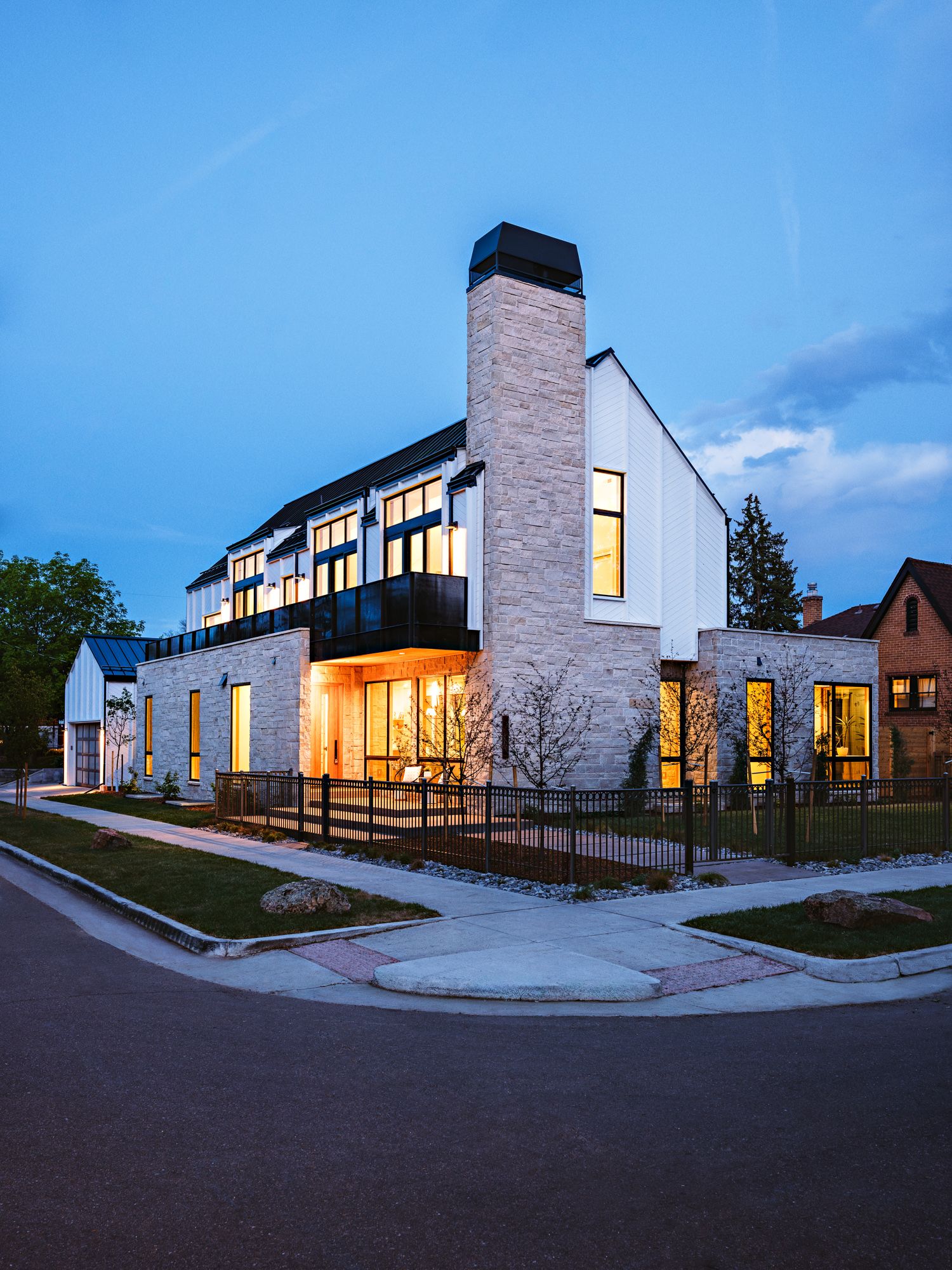 Contemporary two-story home at twilight with stone and white siding, large windows, balcony, and prominent chimney.