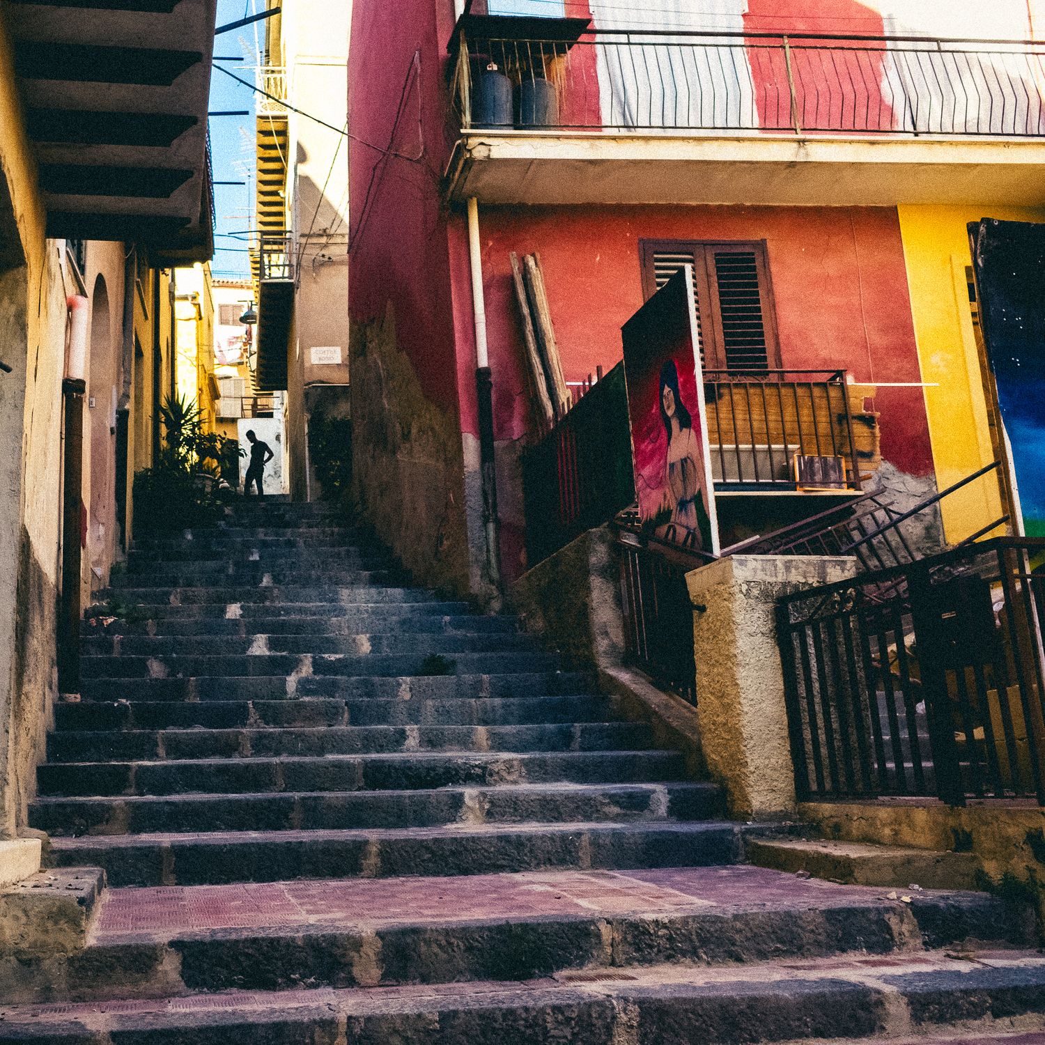 Colorful stone stairway between vibrant red and yellow buildings in an old Mediterranean neighborhood.