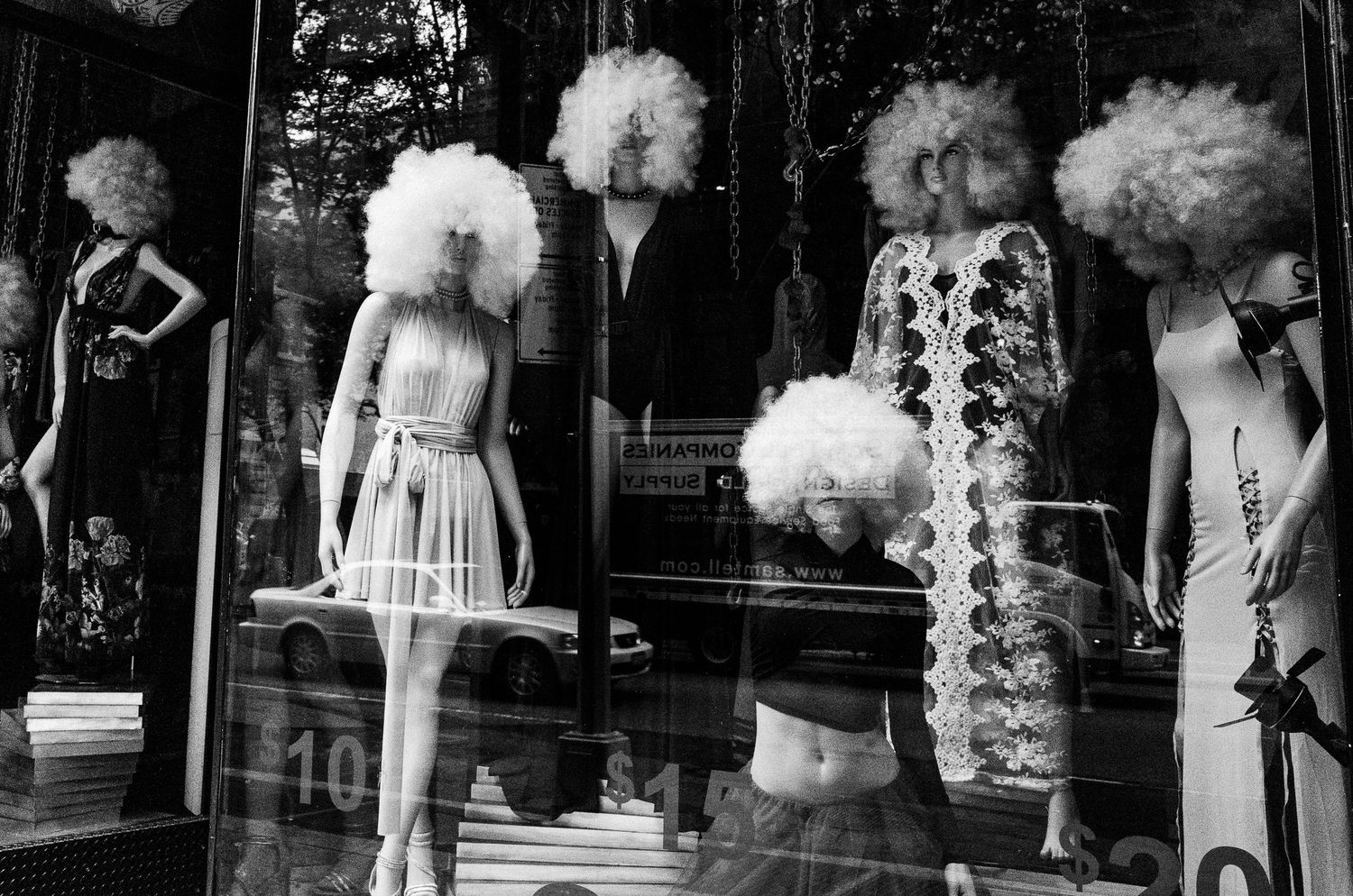 Vintage black and white photograph of mannequins with large white wigs displayed in a store window.