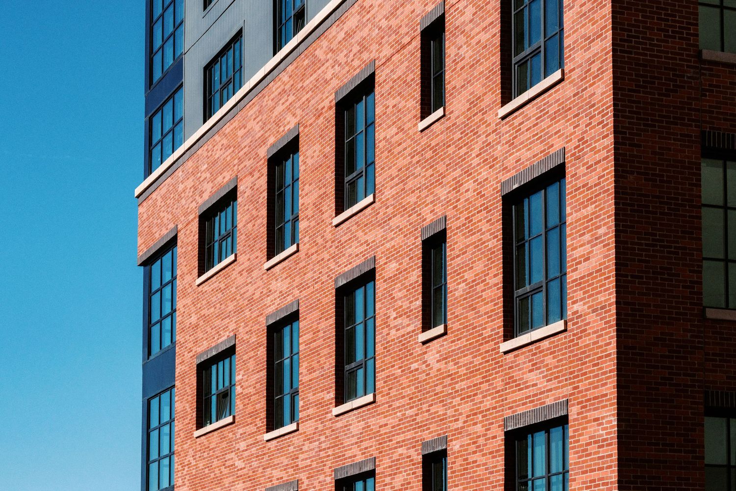 Red brick apartment building facade with black-framed windows against blue sky.