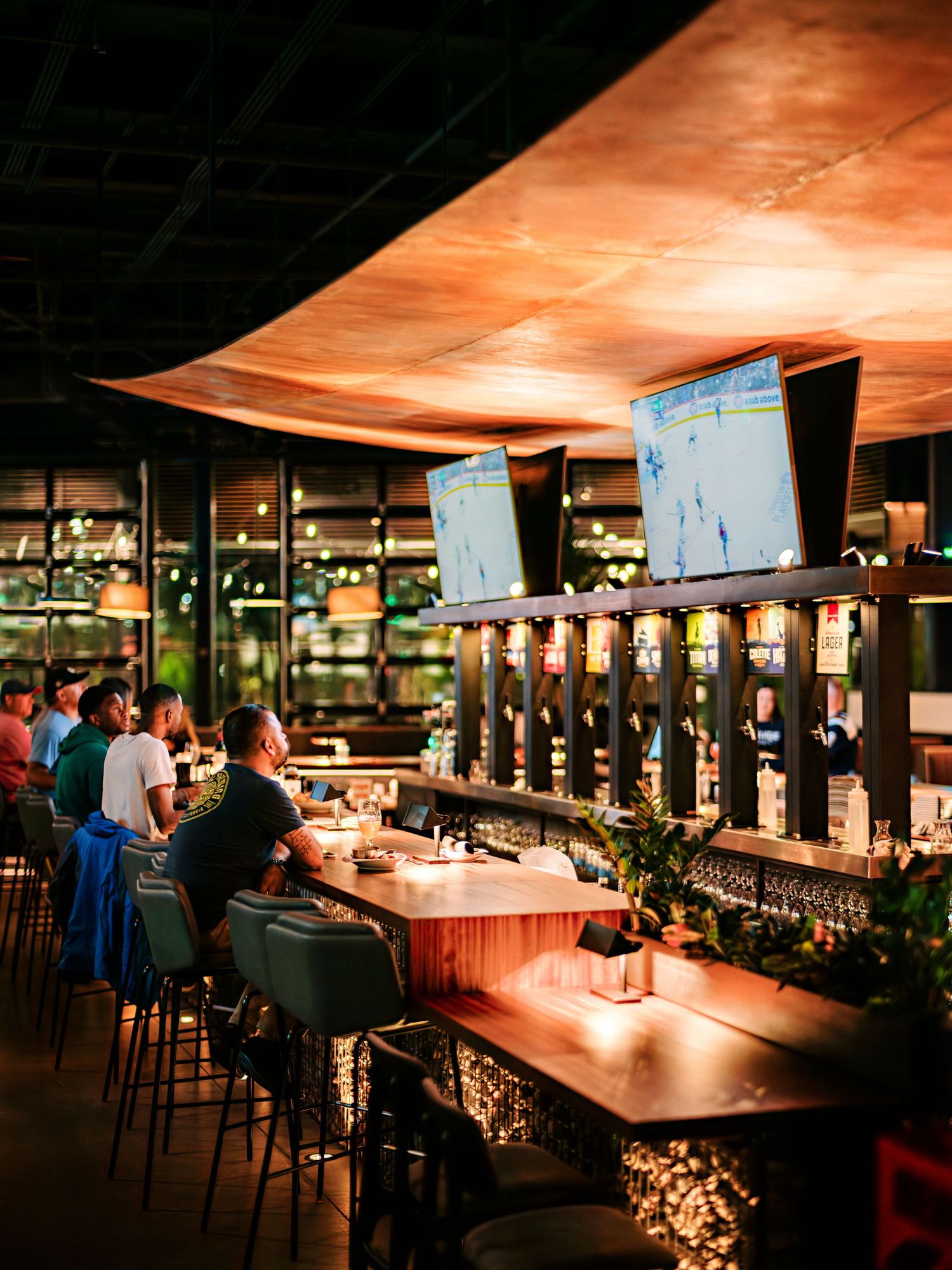 Stylish bar area with illuminated counter and bar stools under warm copper-toned lighting.