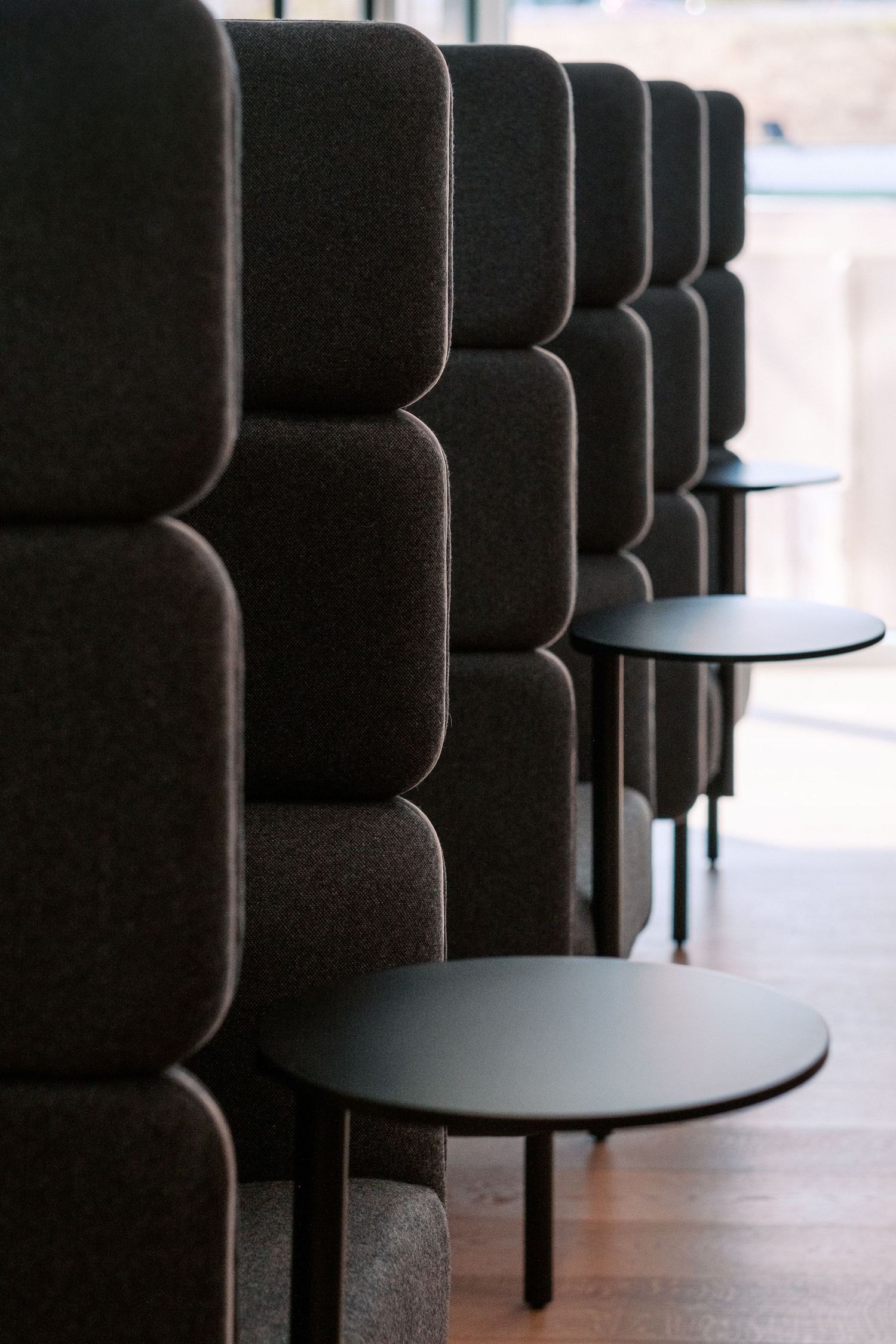 Row of black upholstered booth seating with small round tables in a modern space.