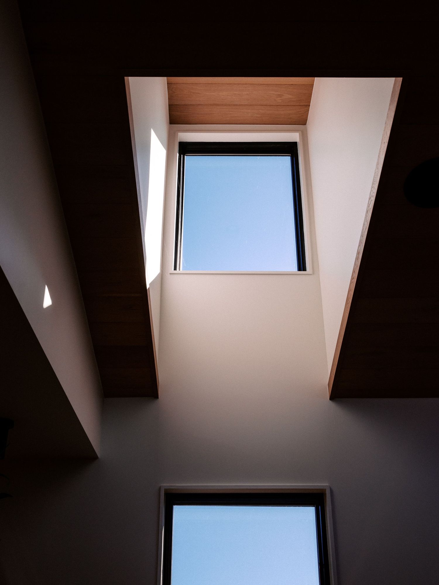 Minimalist skylight windows in dark ceiling creating dramatic angular shadows and light patterns.