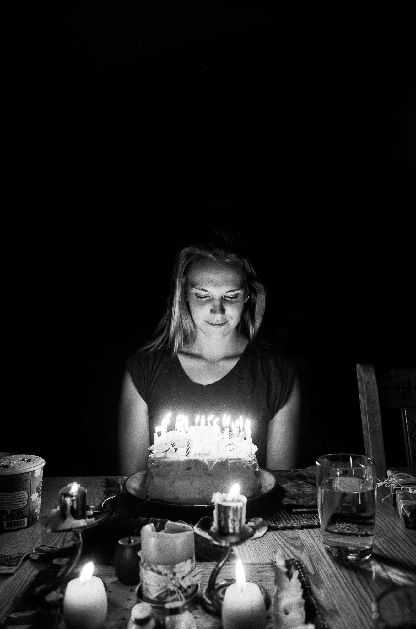 Person illuminated by birthday cake candles in dark room creating intimate lighting.