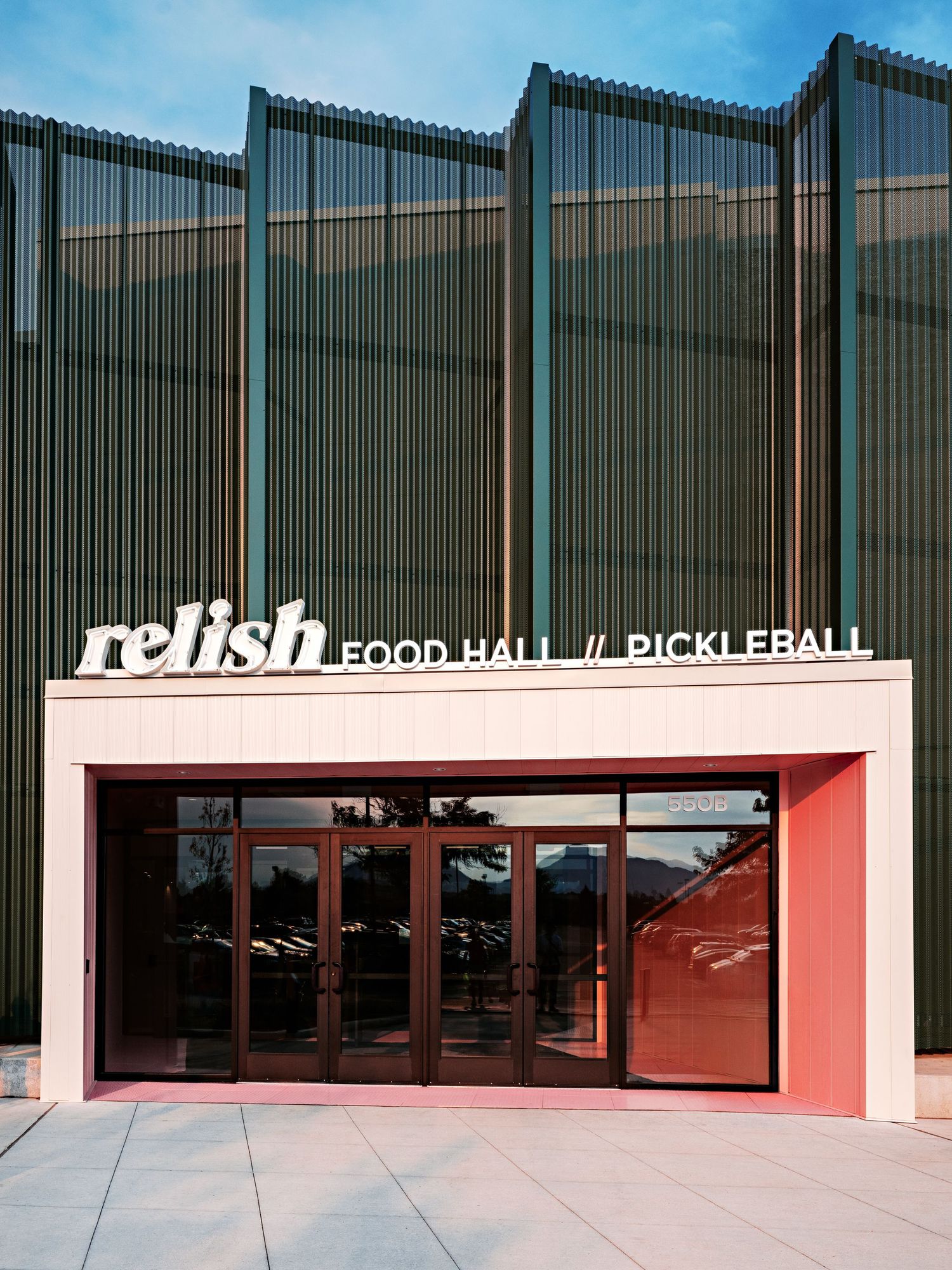 Sports facility entrance with red accent wall displaying 'Food Hall // Pickleball' signage.