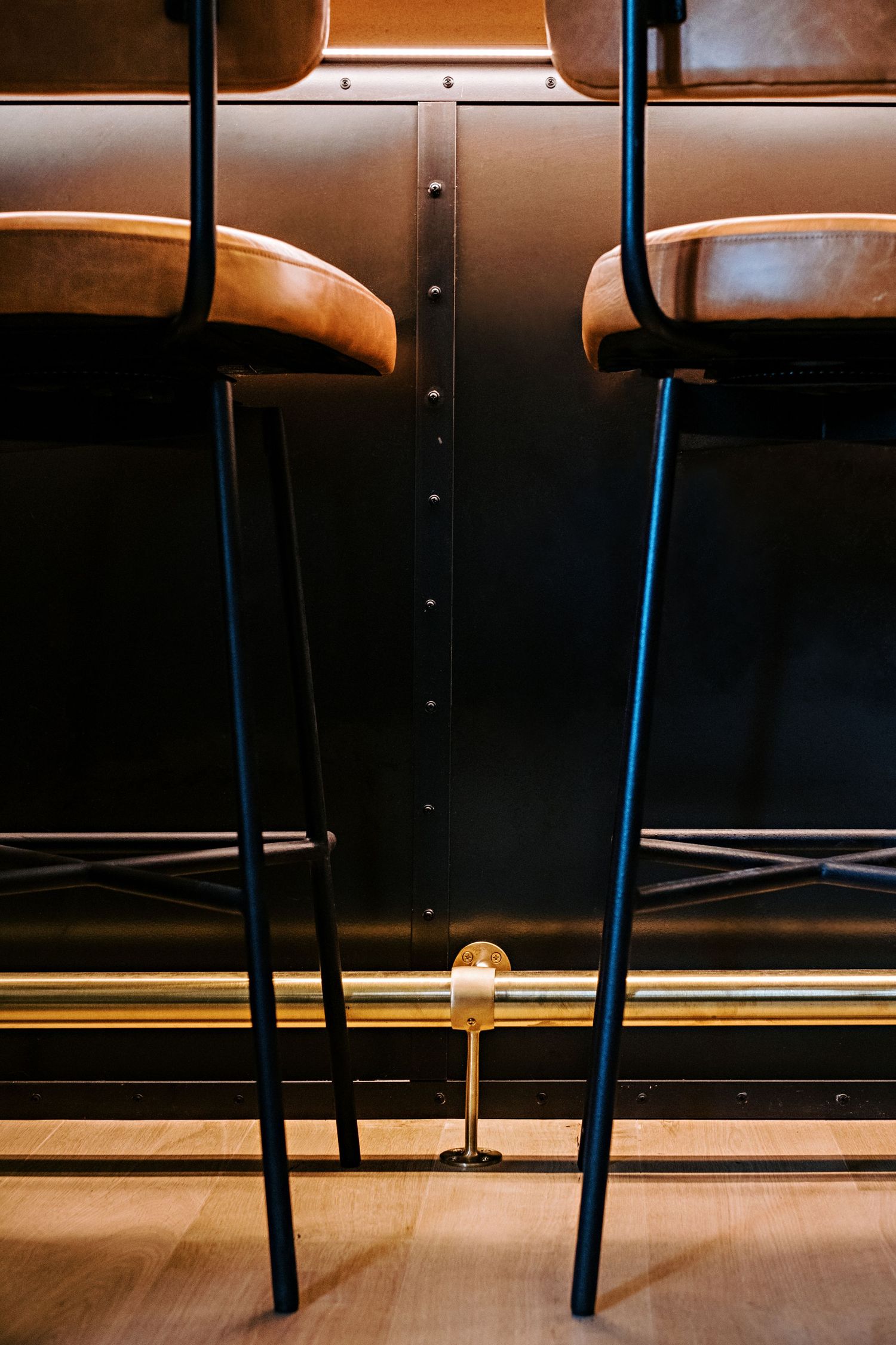 Close-up detail of leather bar stools with black metal frames against wooden flooring.