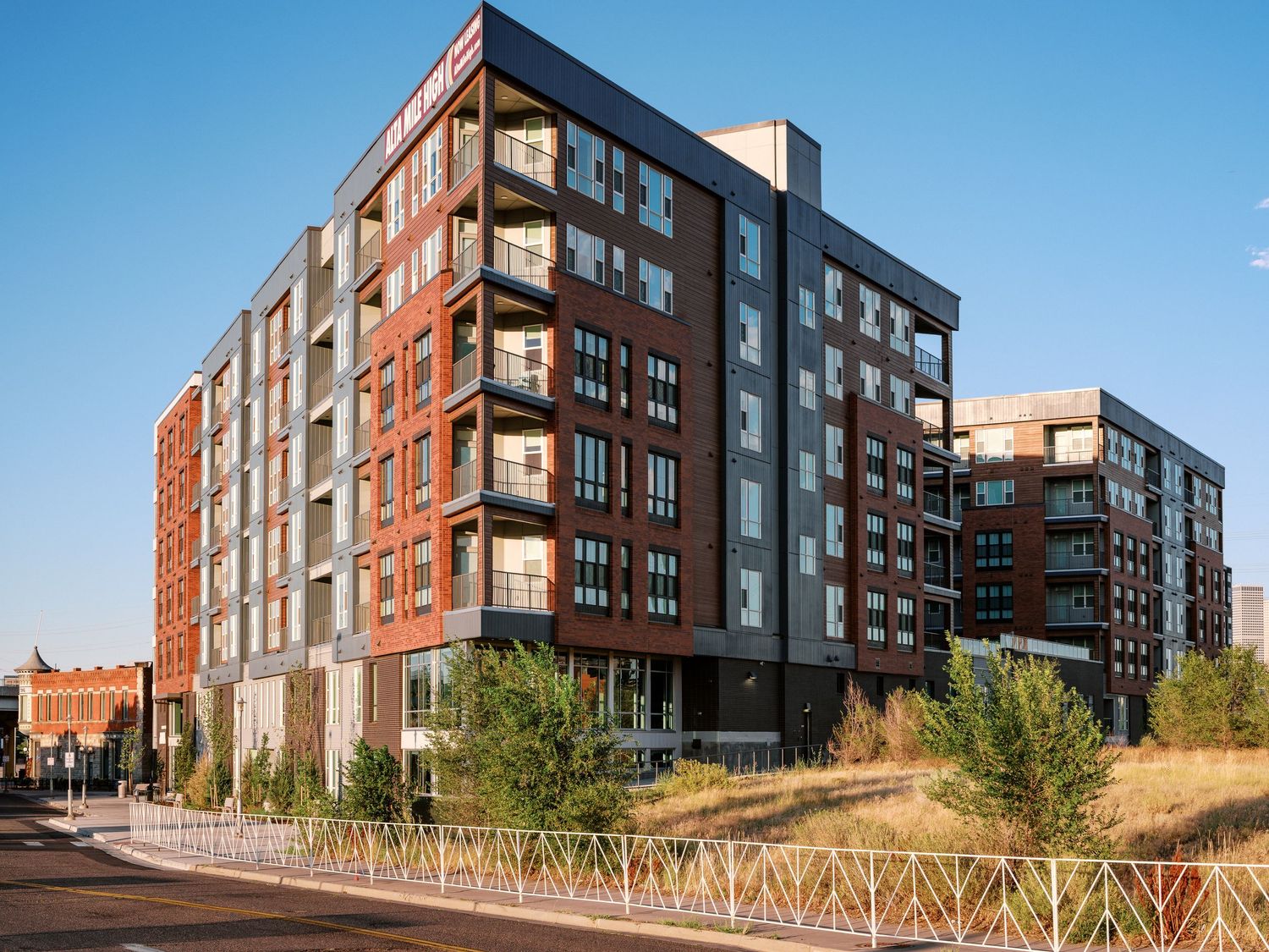 Contemporary multi-story apartment complex with red and gray exterior against blue sky.