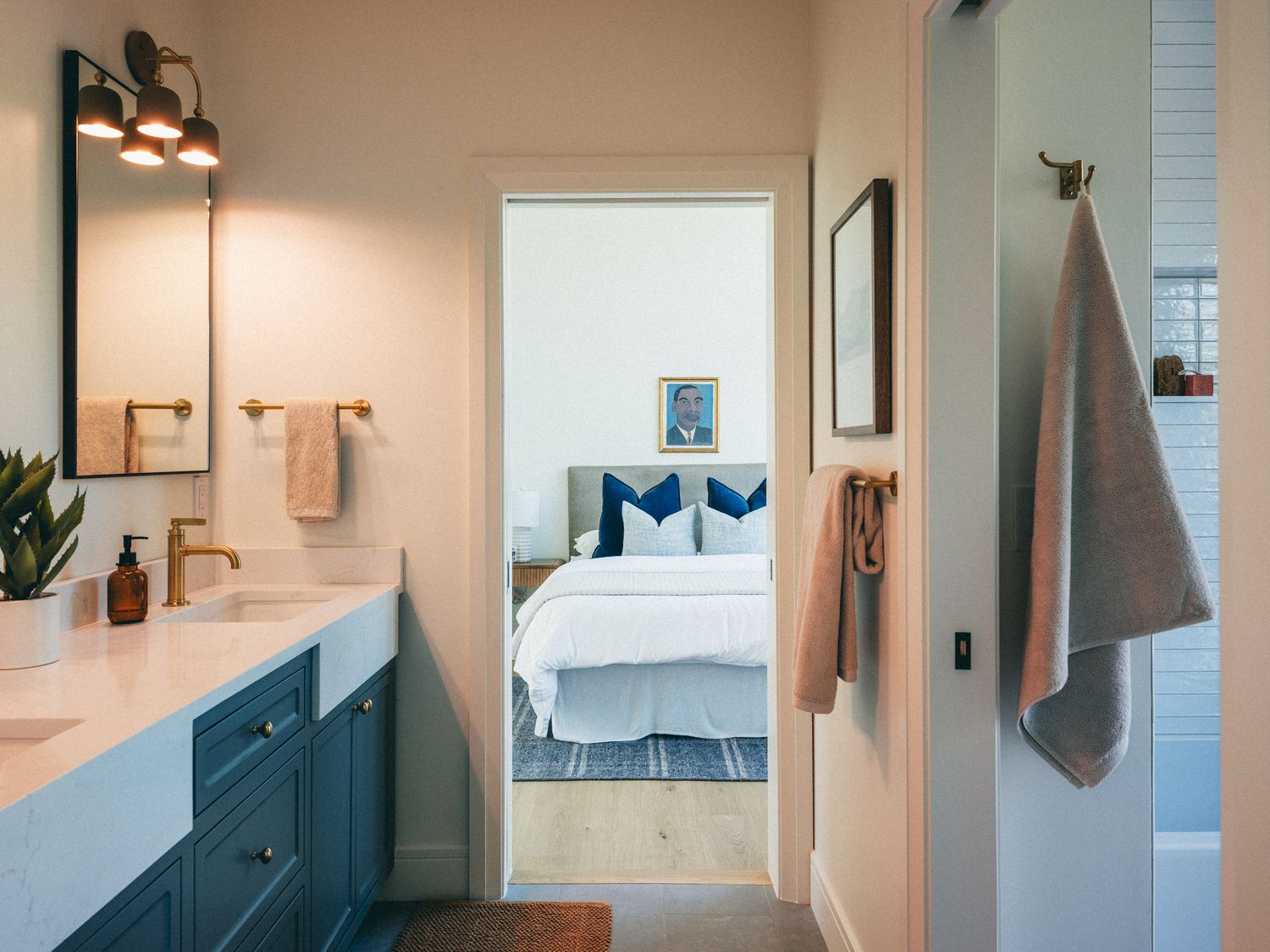 Modern bathroom with teal vanity, gold fixtures, white countertop, and view into a blue and white bedroom.