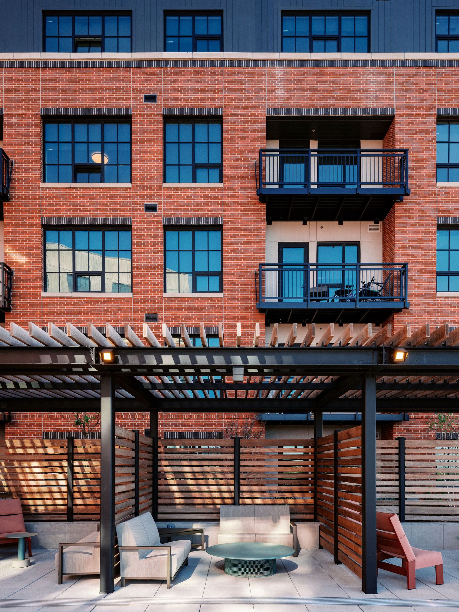 Apartment building exterior with wooden pergola and outdoor seating area.