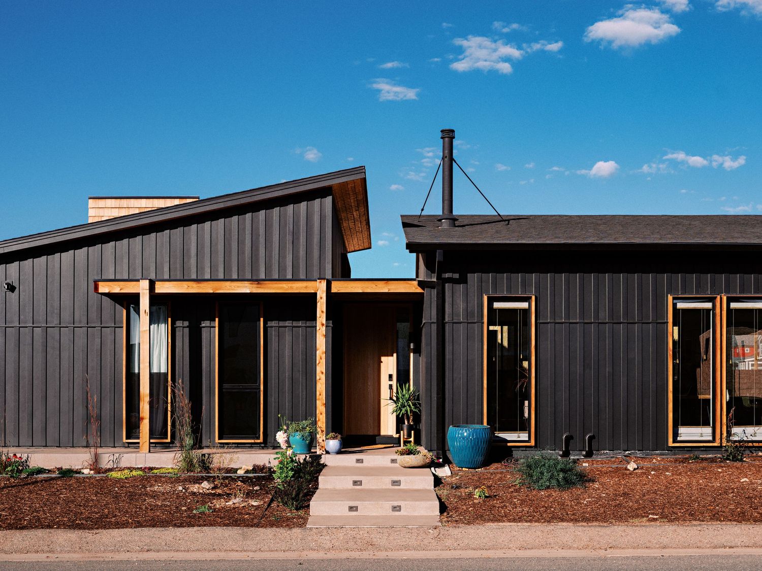Modern dark-colored residential building with wooden accents and large windows under a bright blue sky.