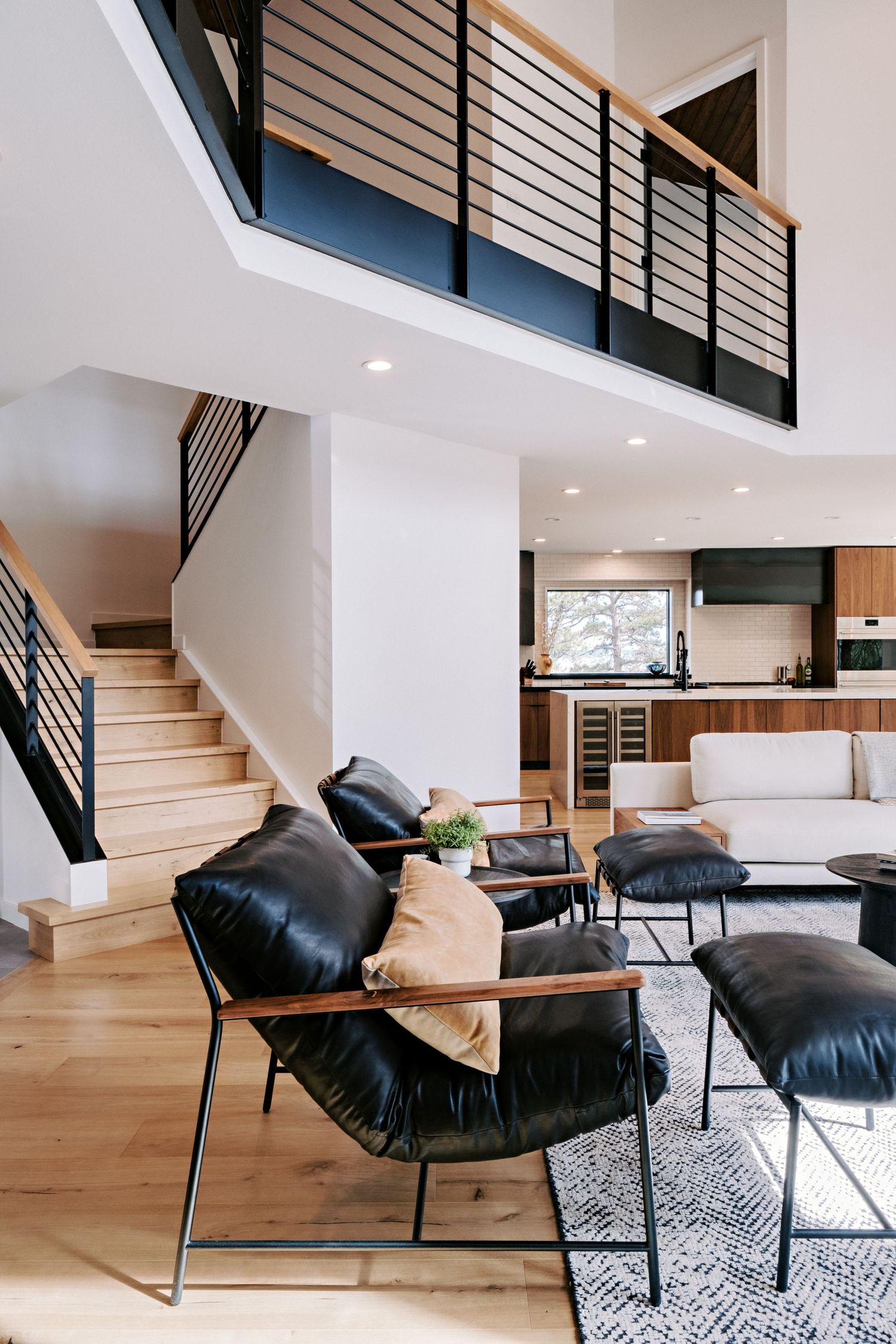 Contemporary living room with black leather lounge chairs and geometric patterned rug on light wood floors.