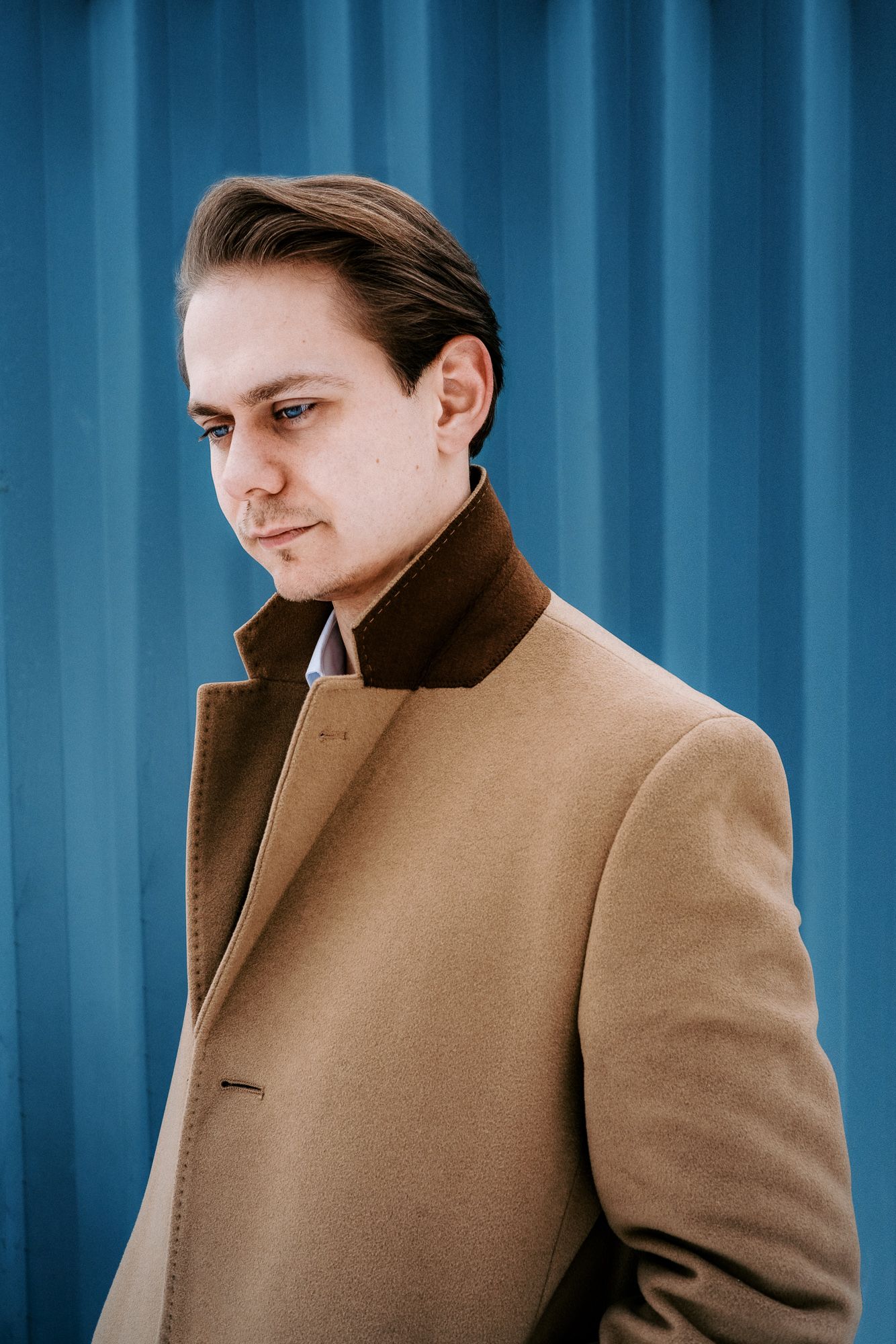 Portrait series showing person in tan coat against blue industrial background.