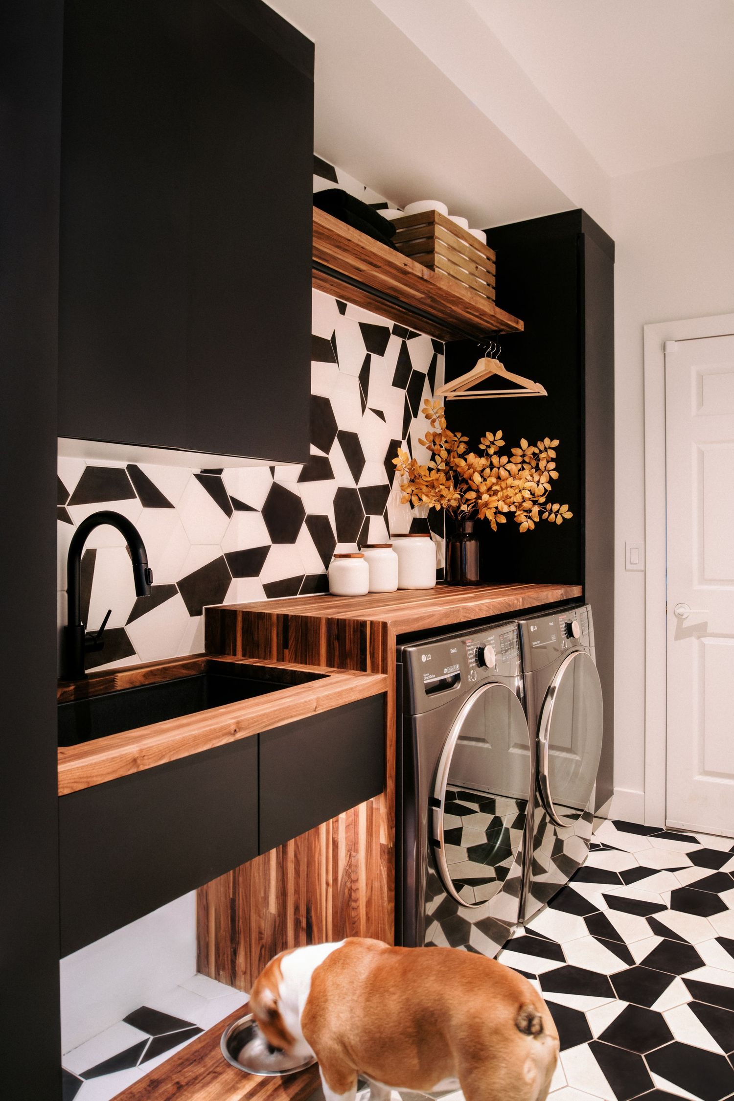 Modern black and white laundry room with geometric floor tiles and wooden countertops.