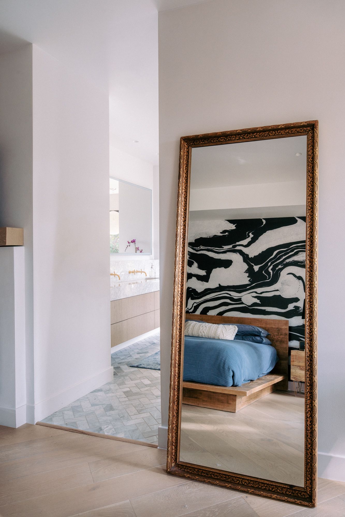 Large ornate gold-framed mirror reflecting a contemporary bedroom with blue accents.