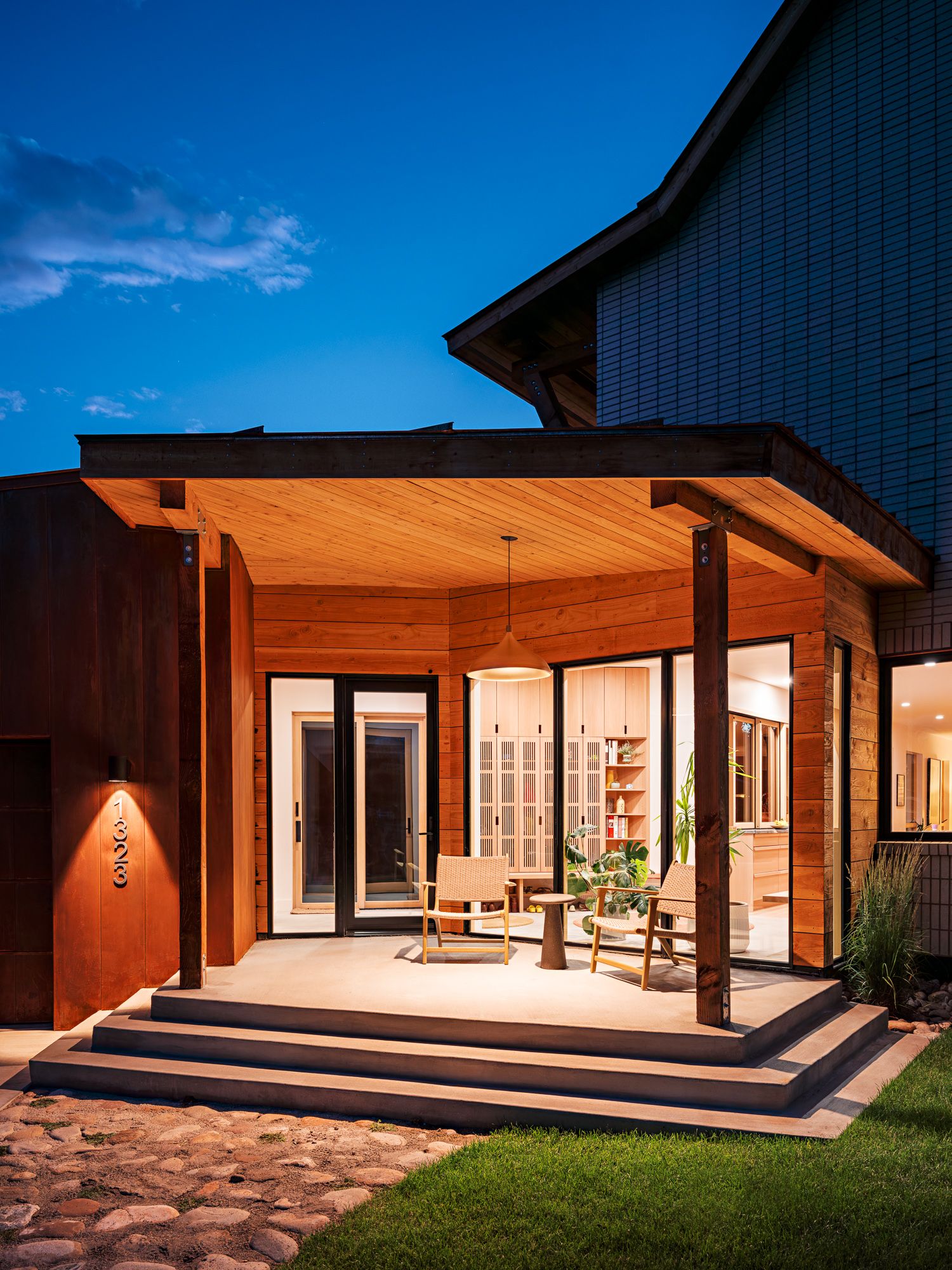Modern wooden house exterior with covered porch and large windows at sunset.
