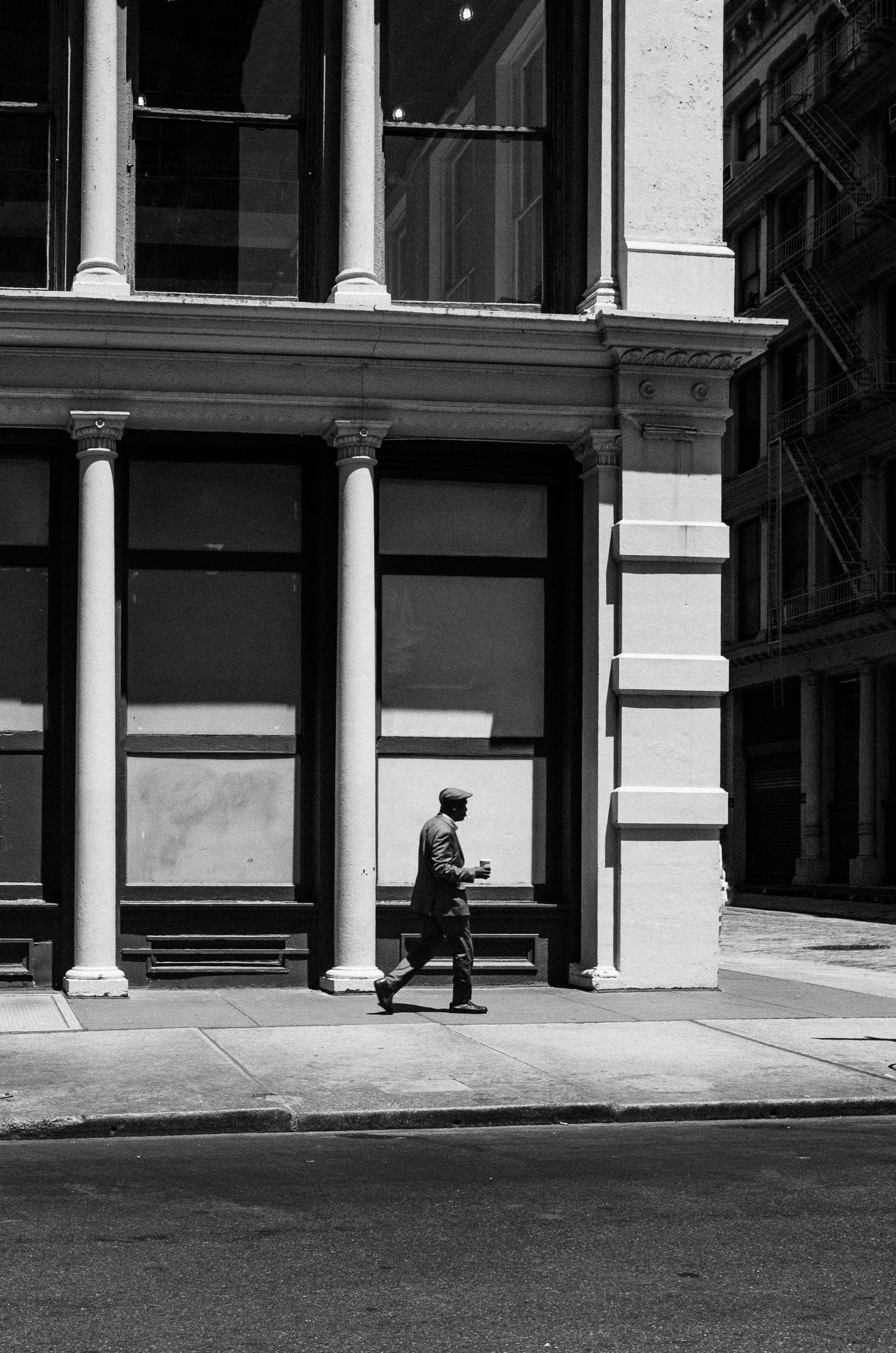 A person walks past a classical building facade with white columns and architectural details in black and white photography.