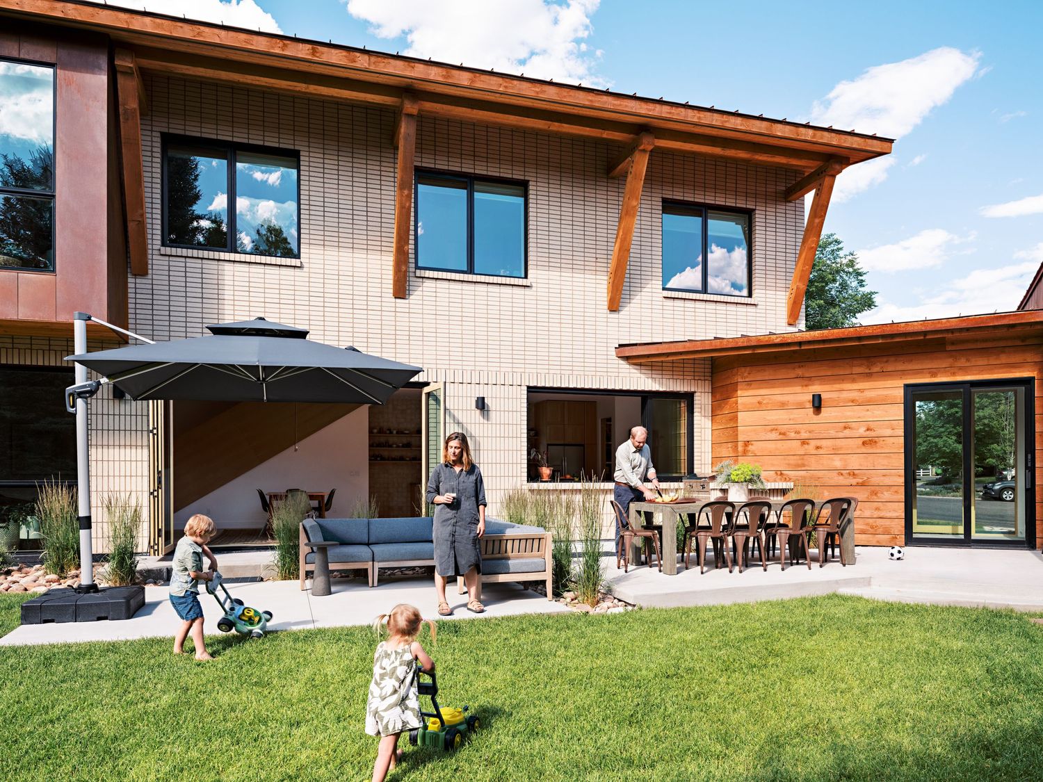 Contemporary house exterior with wood siding and large windows set against green lawn and blue sky.