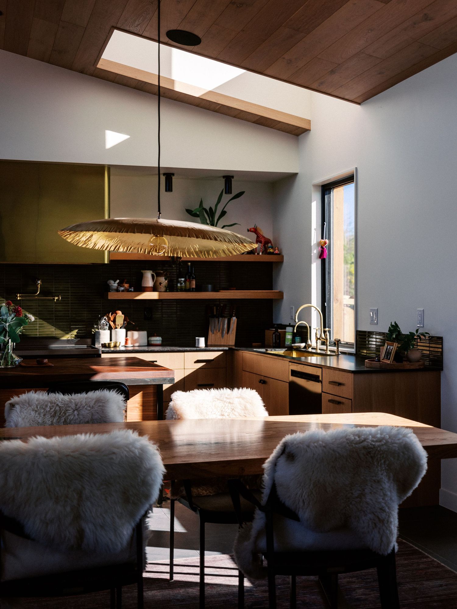 Cozy dining space with plush grey fur chairs and wooden table under natural lighting from skylights.