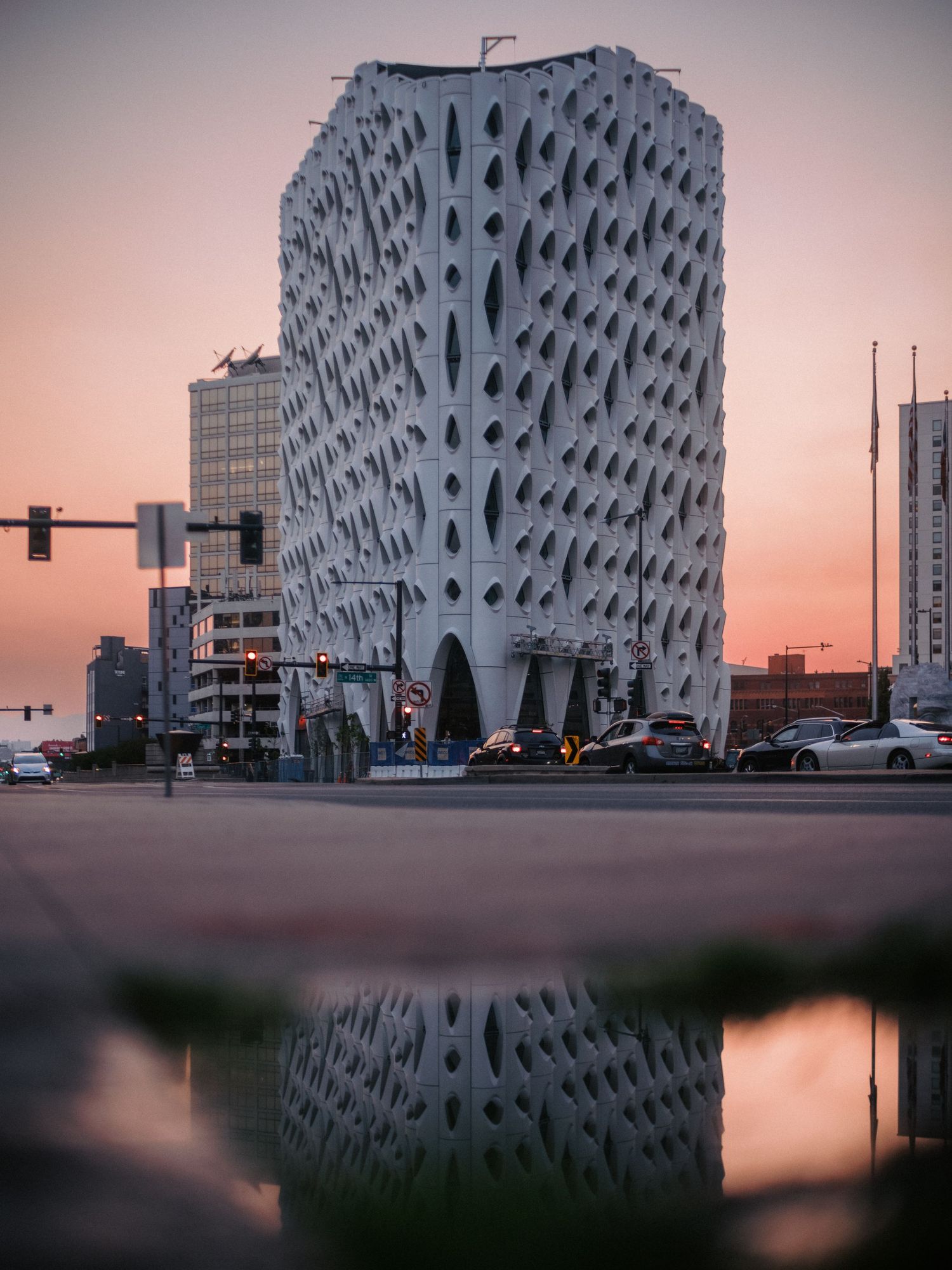 Geometric white building with distinctive honeycomb pattern facade reflecting in still water at dusk.