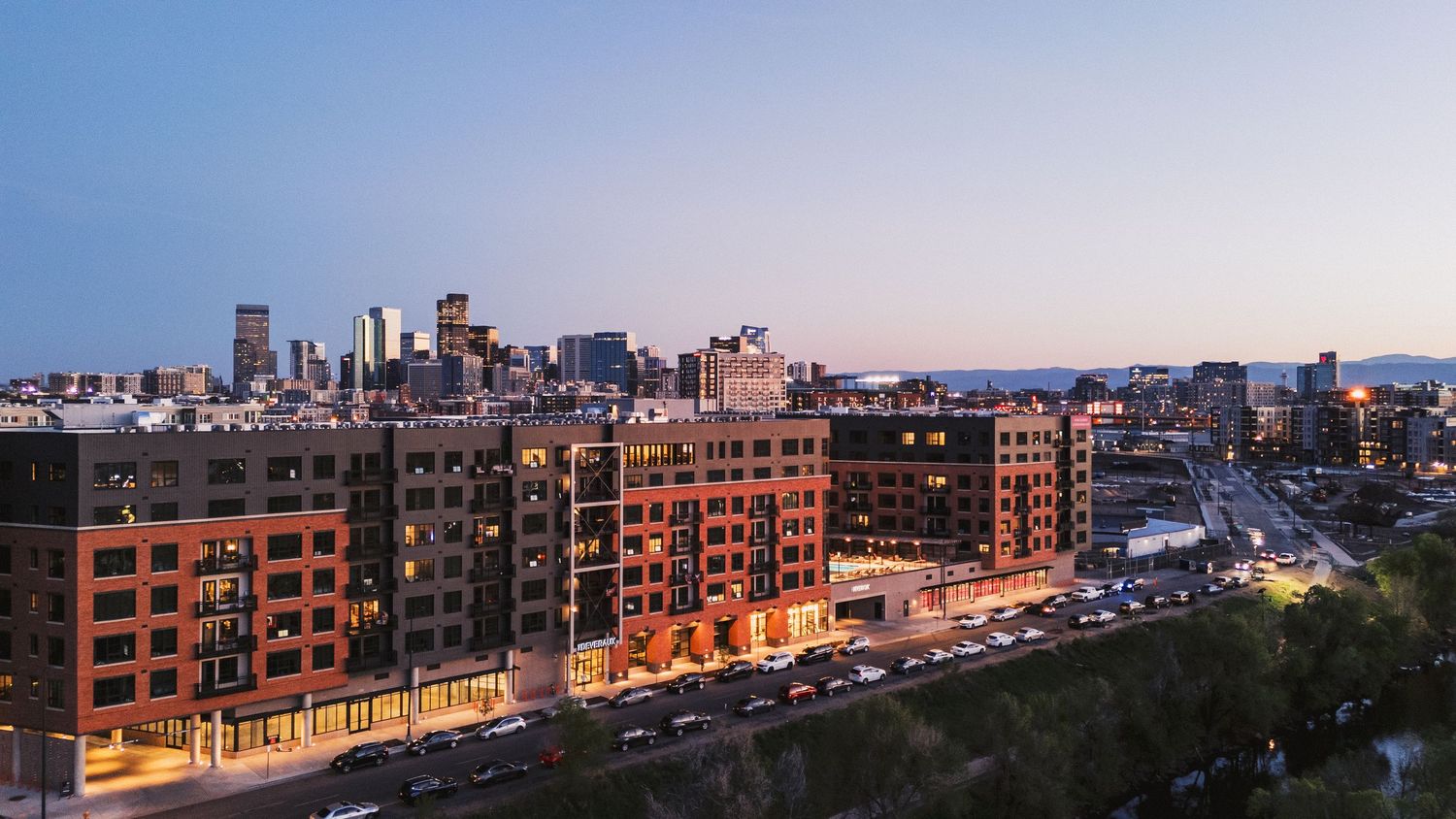 Panoramic cityscape view of downtown buildings at dusk with orange sky.