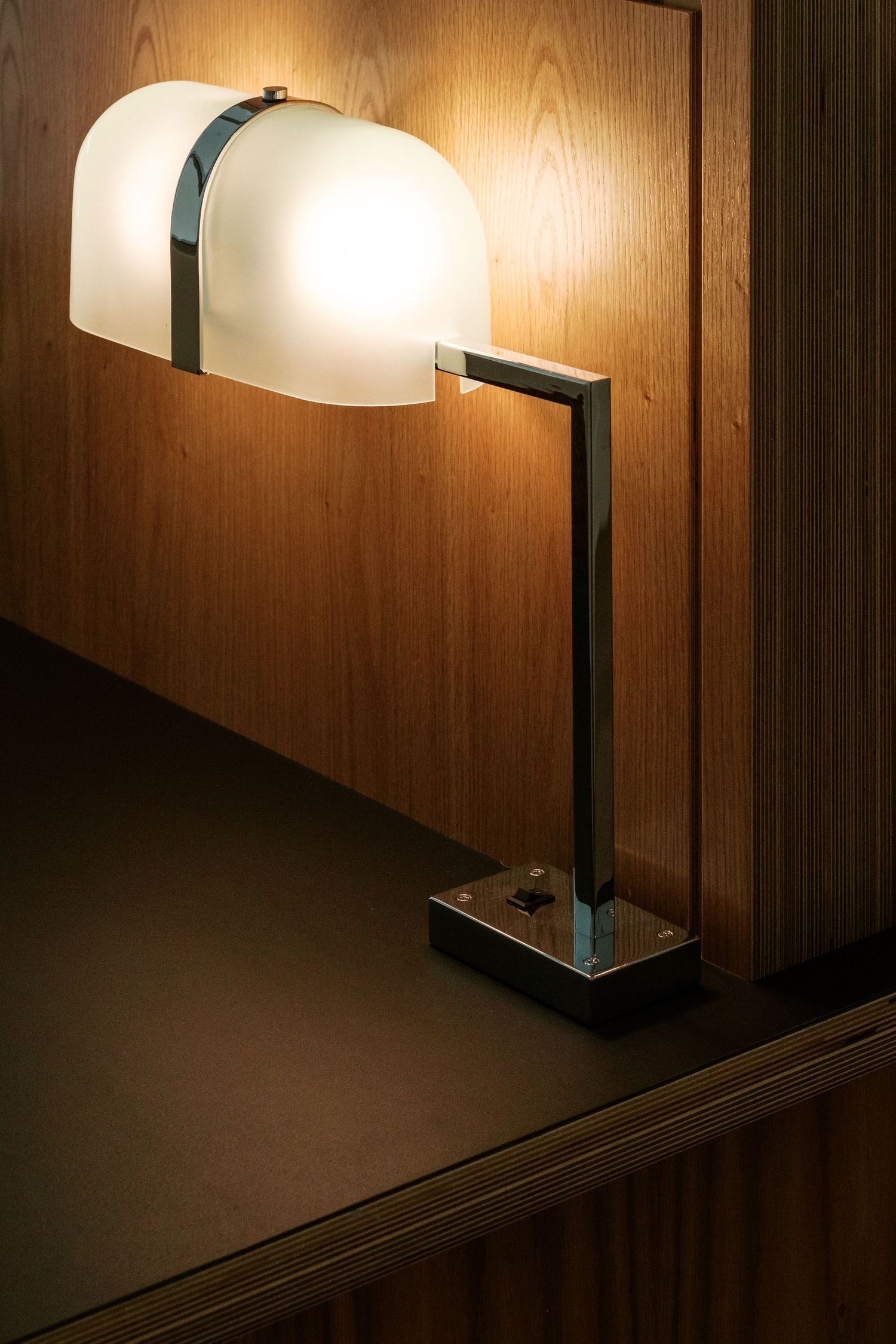 Close-up of a sleek desk lamp with wood paneling and ambient lighting.