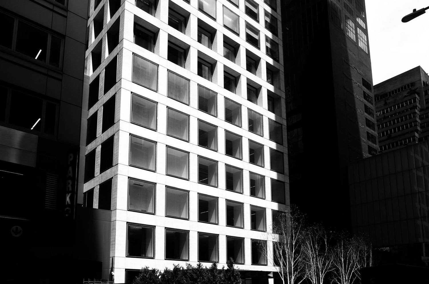 Black and white architectural photo of a modern office building with grid-like windows and a helicopter flying overhead.