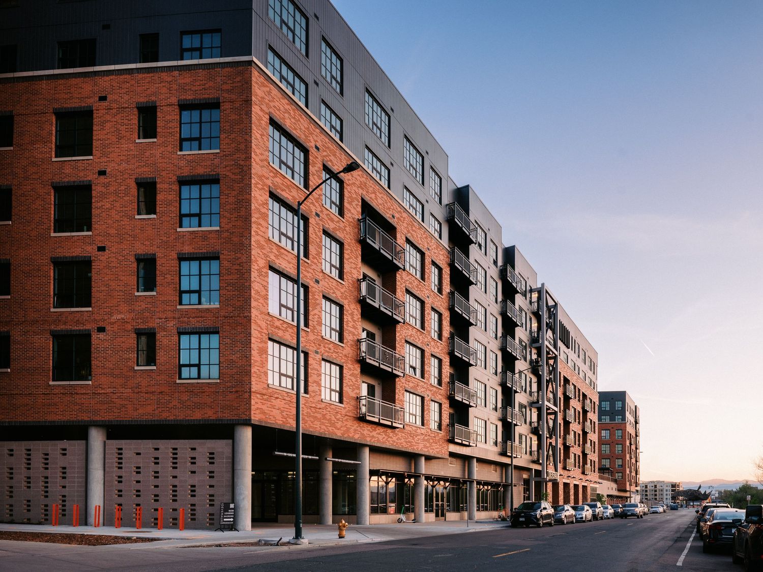 Modern red brick apartment building with balconies stretching along a street view.