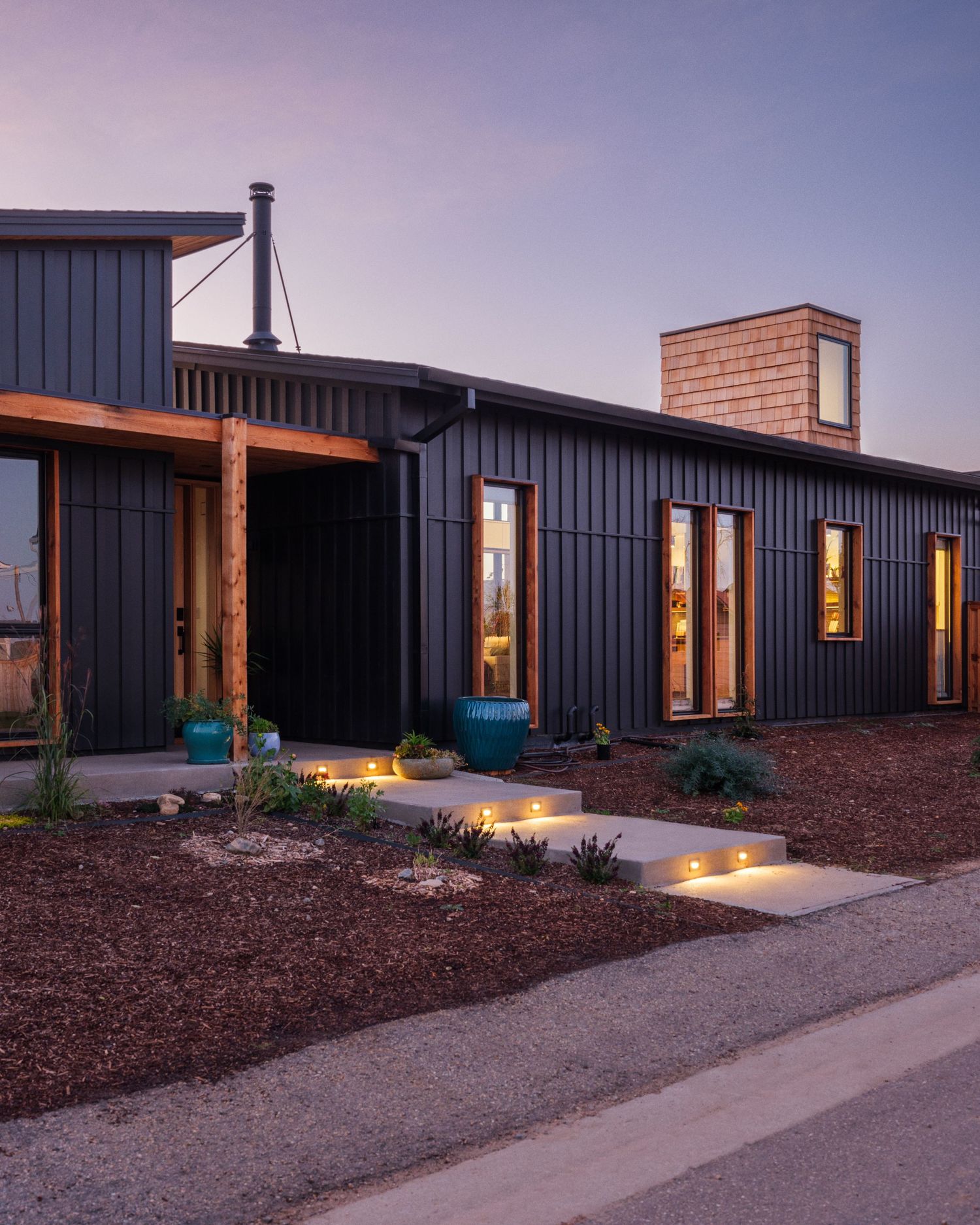 Evening exterior of modern home with illuminated landscape lighting and dark siding.
