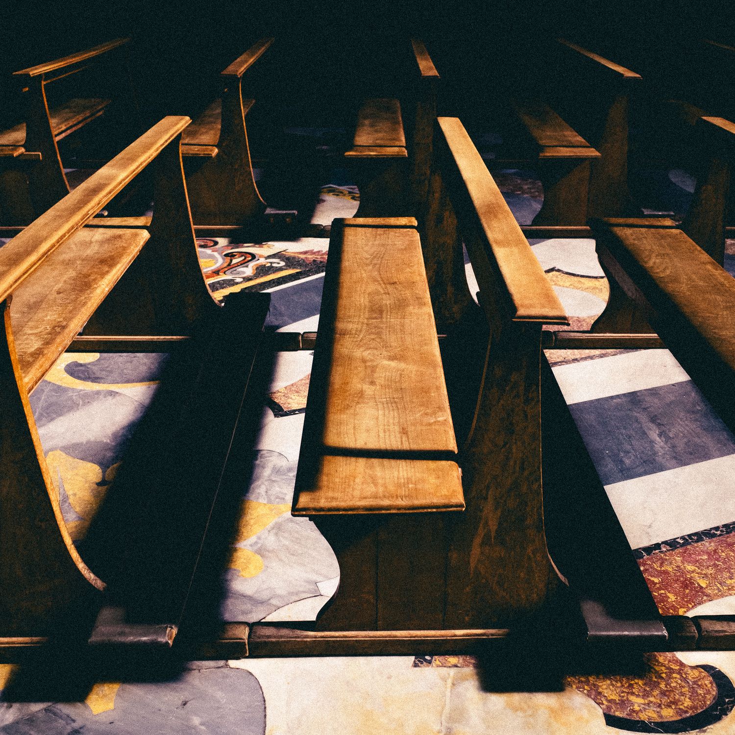 Wooden church pews in a row cast dramatic shadows across a sunlit floor in a historic sanctuary.