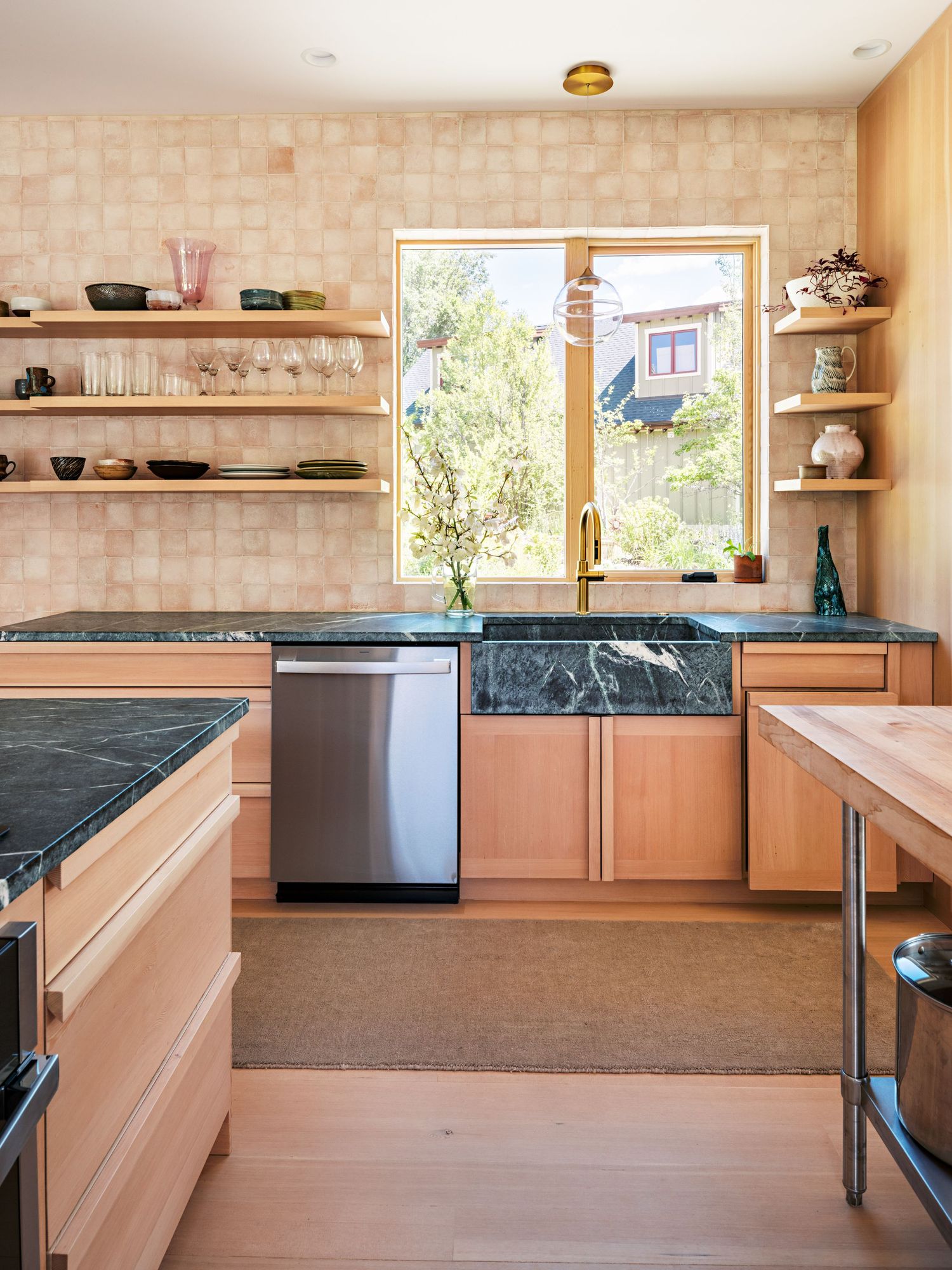 Modern kitchen featuring natural wood cabinets, black countertops and tiled backsplash with open shelving.