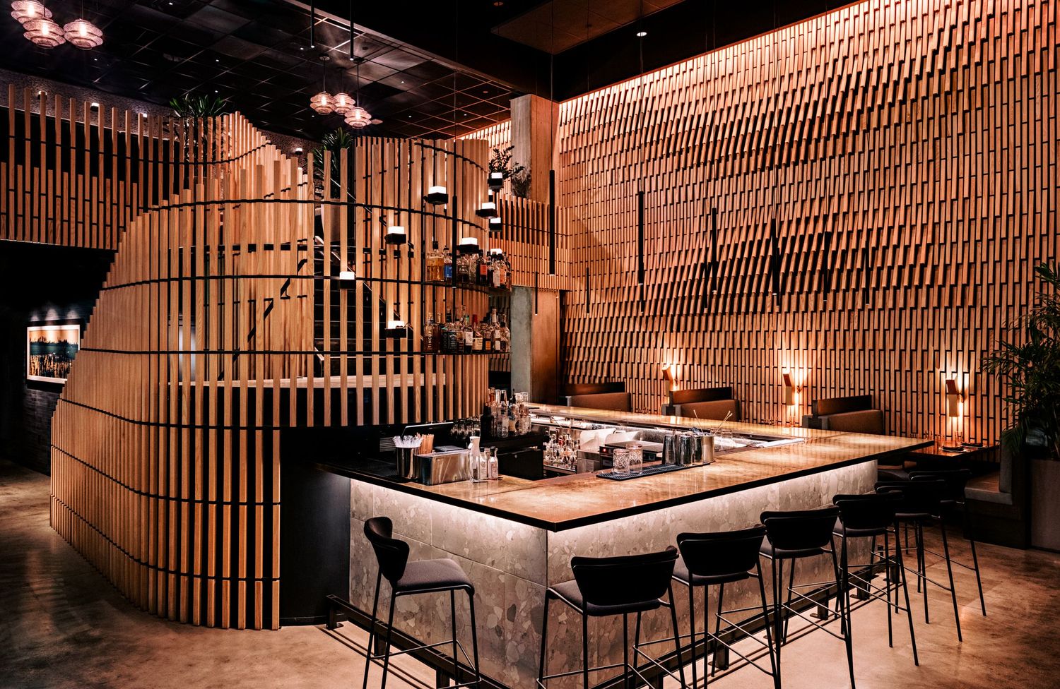 Stylish bar area with curved wooden slat wall design and intimate lighting creating warm ambiance.