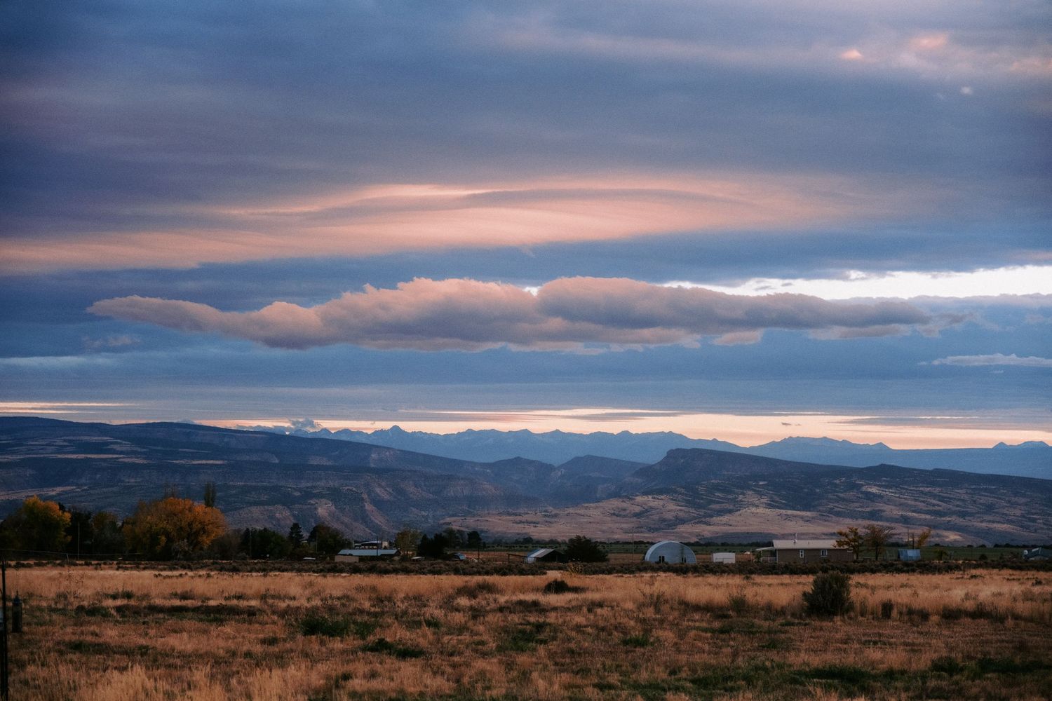 Panoramic mountain vista with dramatic cloud formations at sunset across a vast landscape.