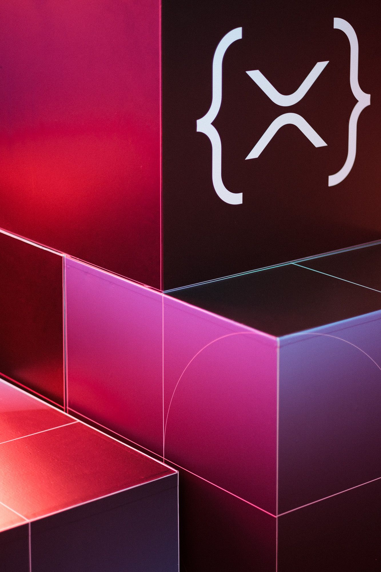 Abstract red and pink glossy 3D cubes with XRP Ripple cryptocurrency logo in curly braces on dark background.