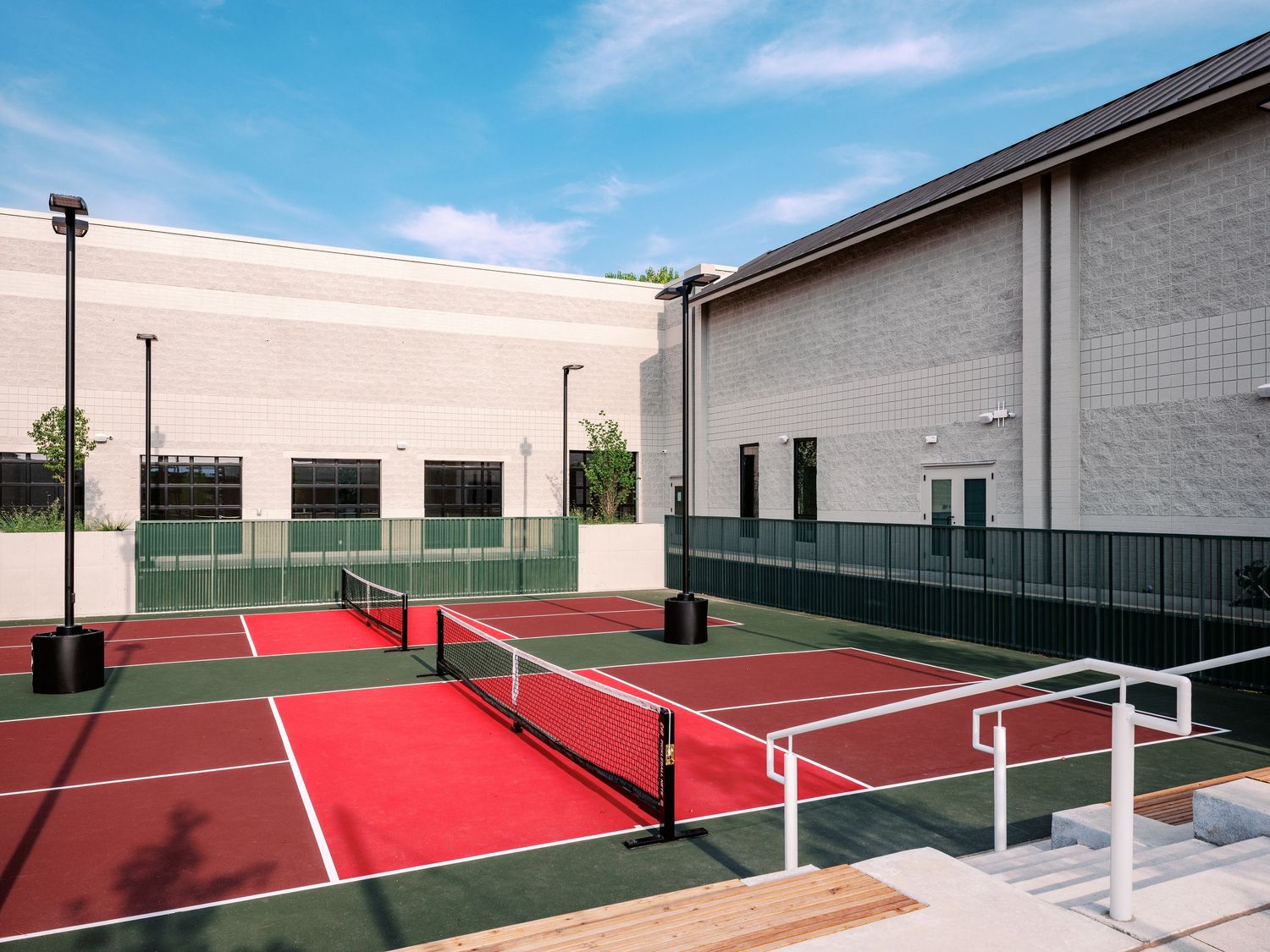 Modern outdoor tennis courts with red playing surfaces and white lines surrounded by high walls.