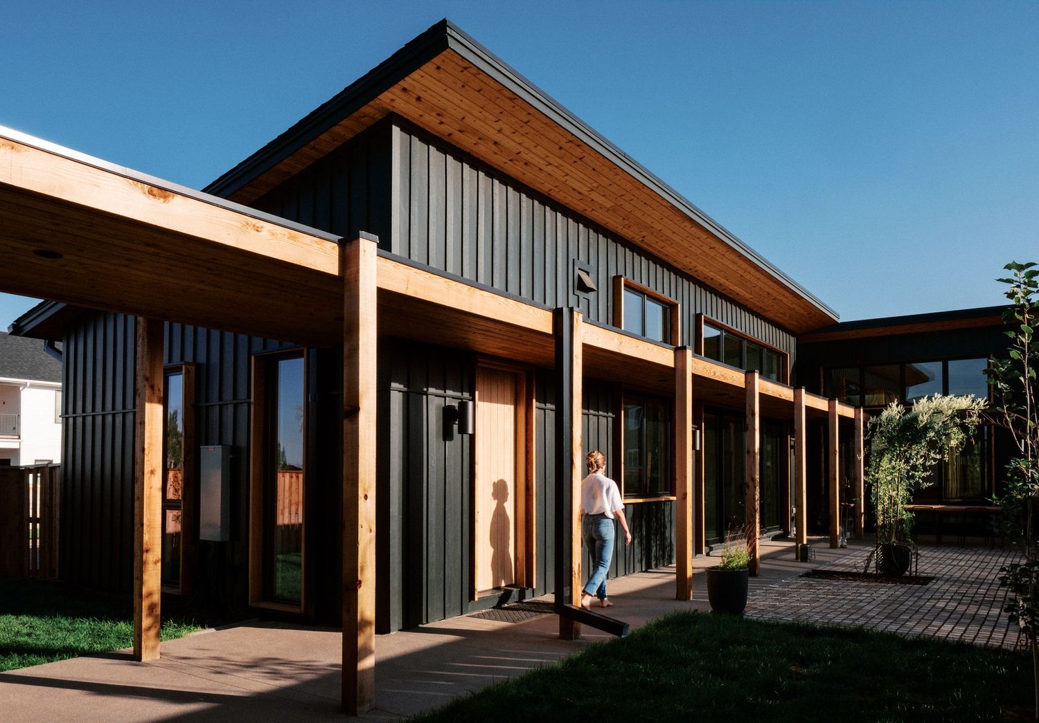 Exterior view of modern house with dark metal siding and wooden overhangs against blue sky.