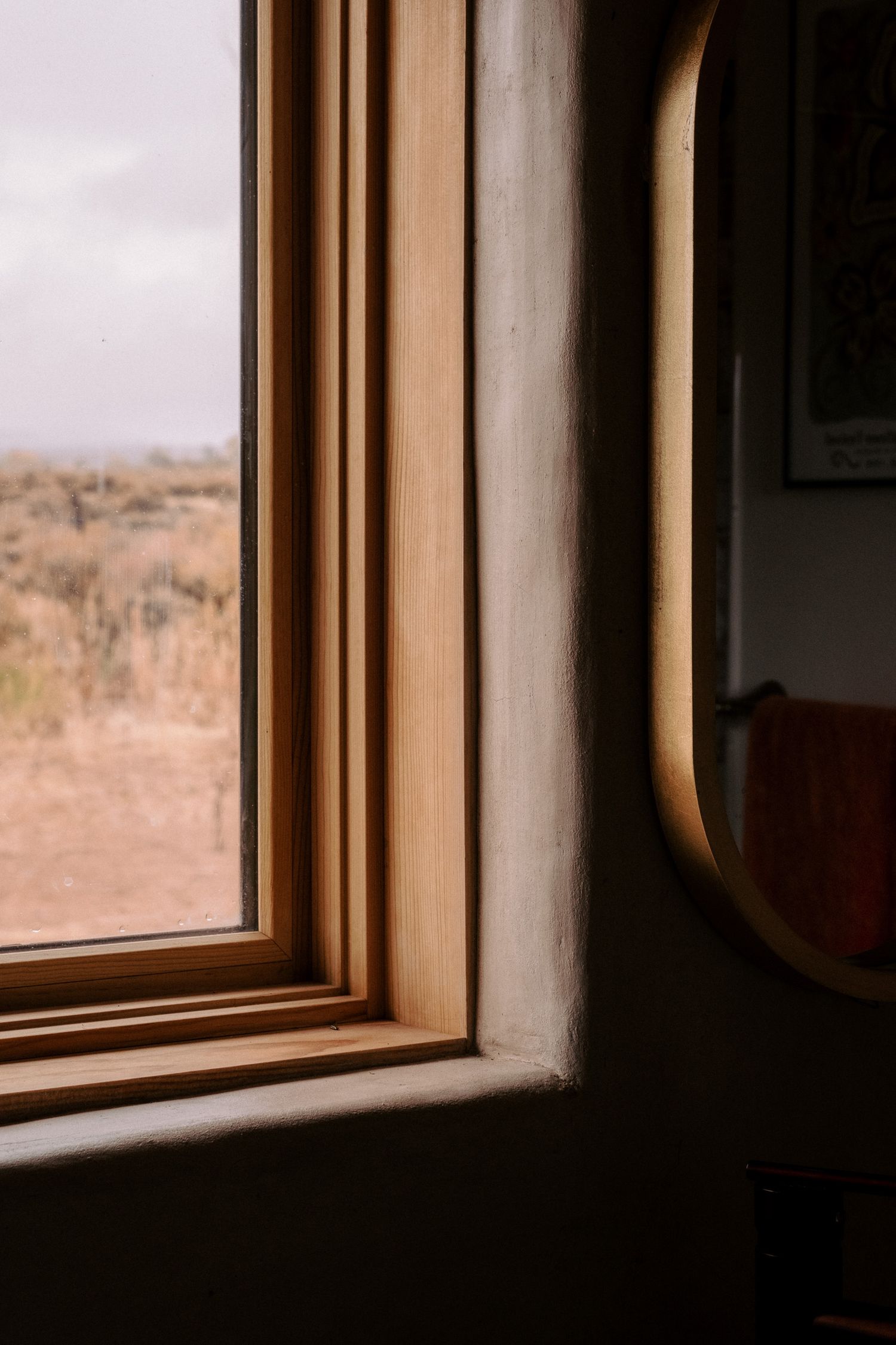 Close-up of wooden window frame with desert landscape visible through glass and curved mirror edge.