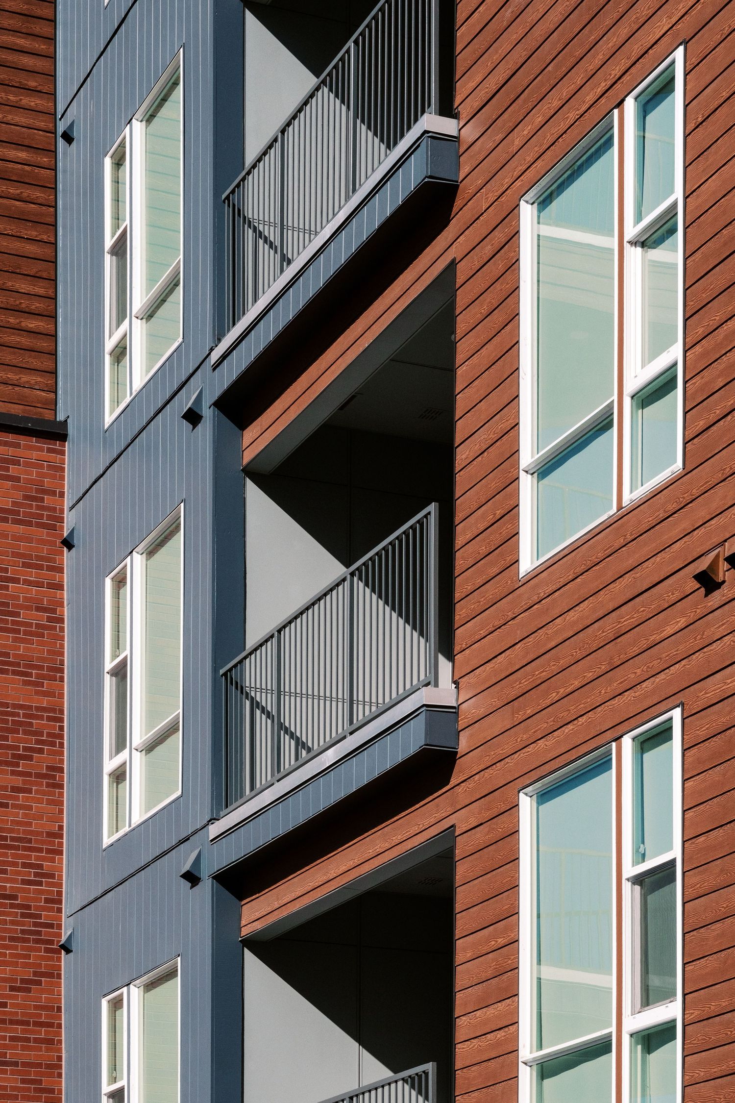 Modern apartment building facade with red brick and gray panels.