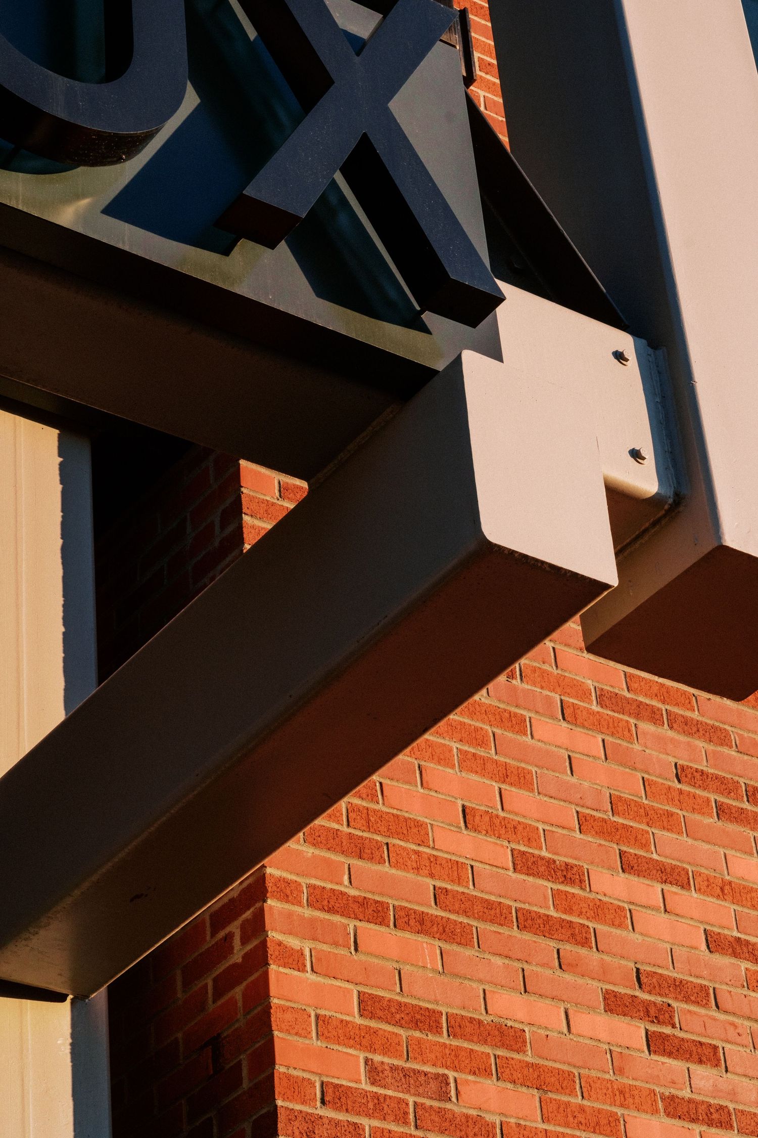 Modern architectural detail showing black metal beams against a red brick wall creating geometric shadows.
